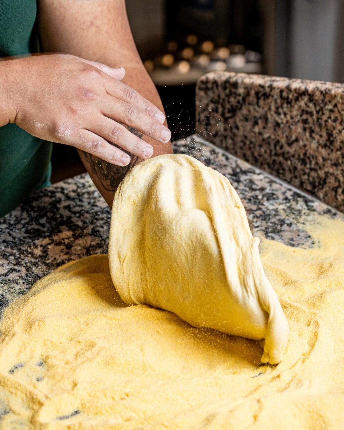 Hands stretching pizza dough through semolina flour on a granite counter
