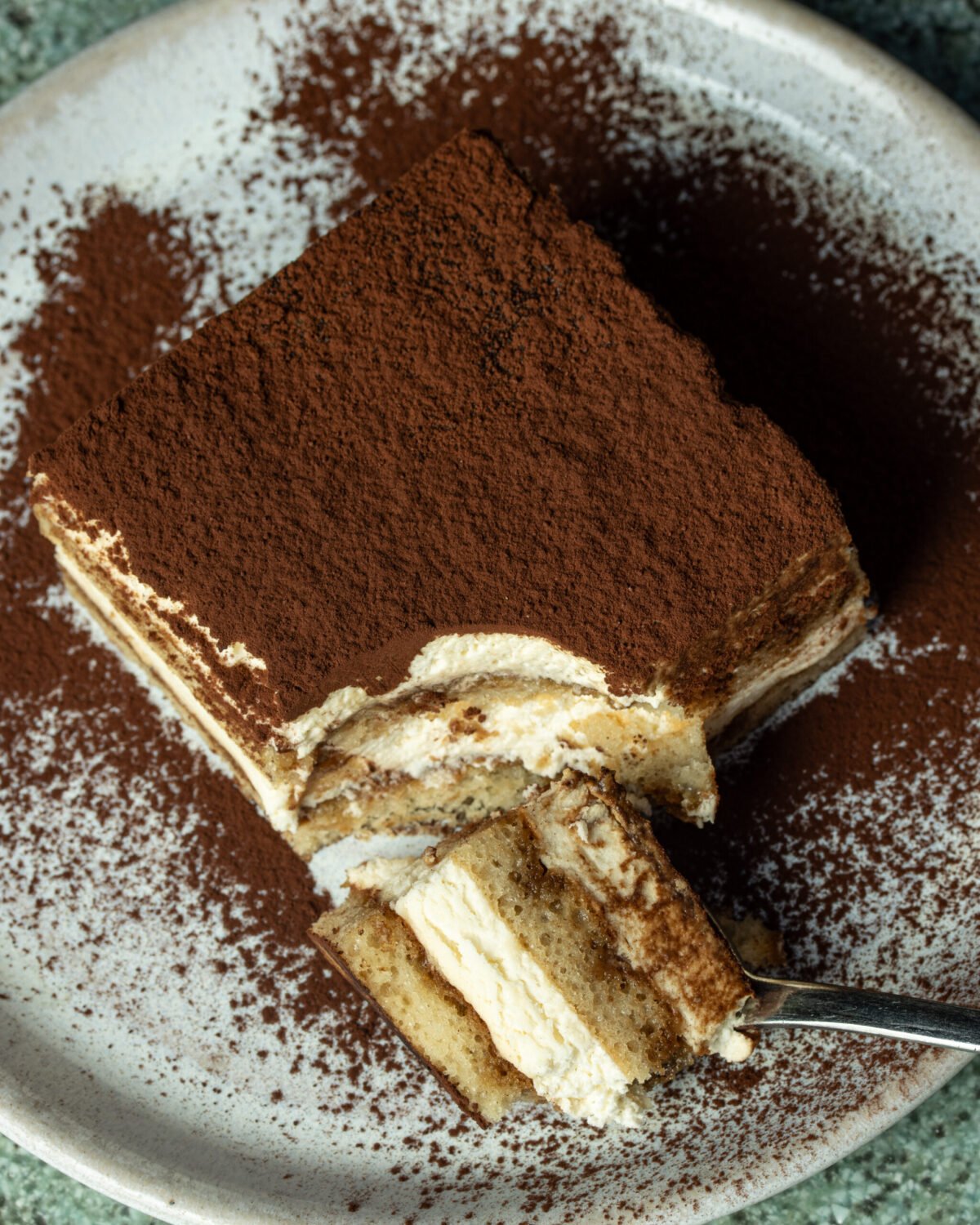 Close-up of tiramisu dusted with cocoa, a forkful lifted from the corner