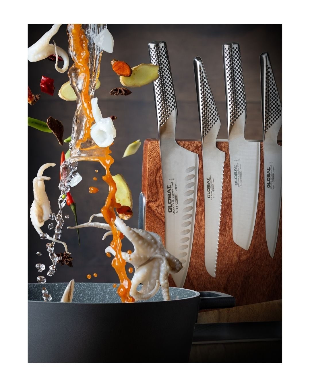 Global chef's knives in a wooden block with squid, ginger and chilli frozen mid-air above a pan