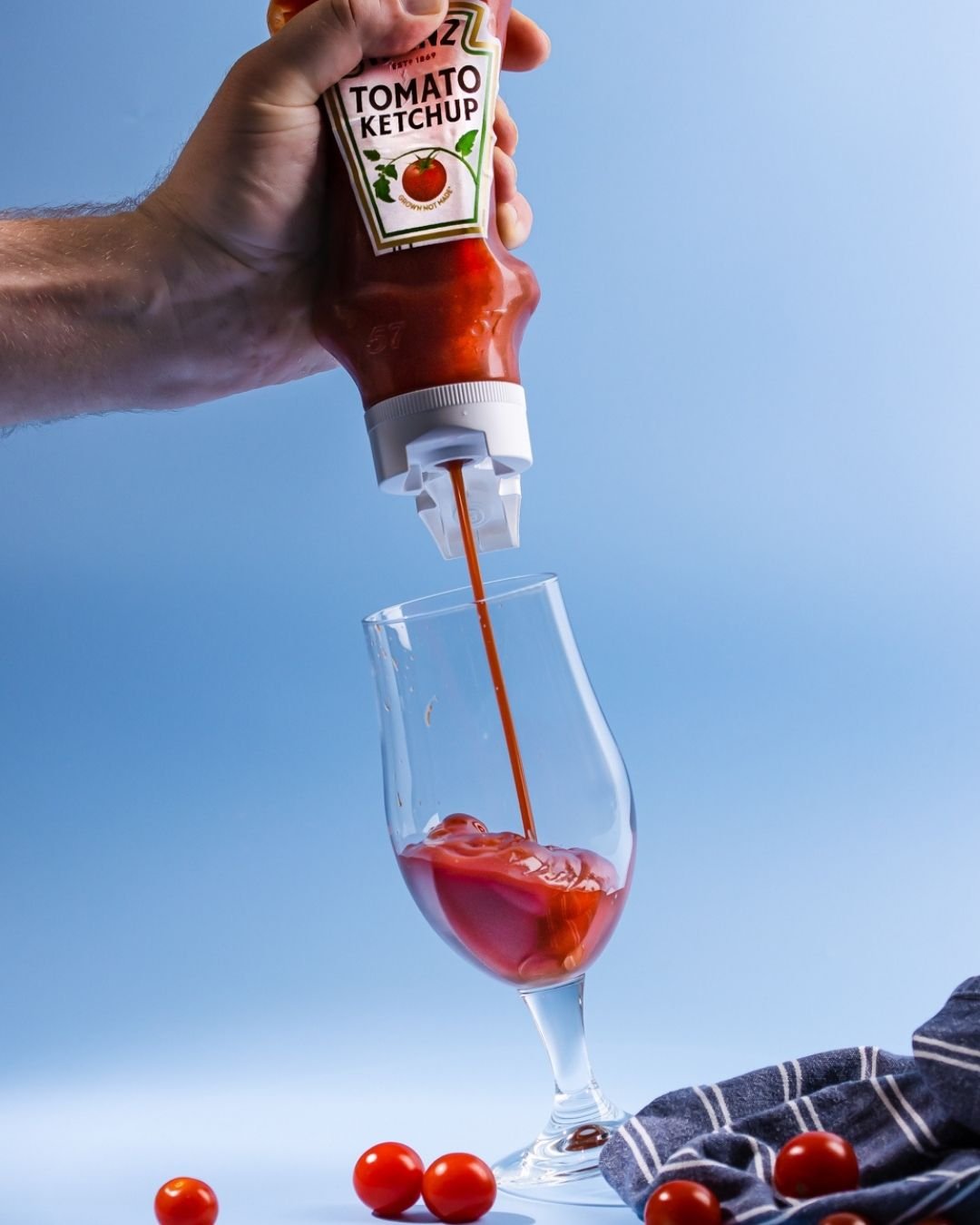 Tomato ketchup squeezed from a bottle into a wine glass, cherry tomatoes scattered below