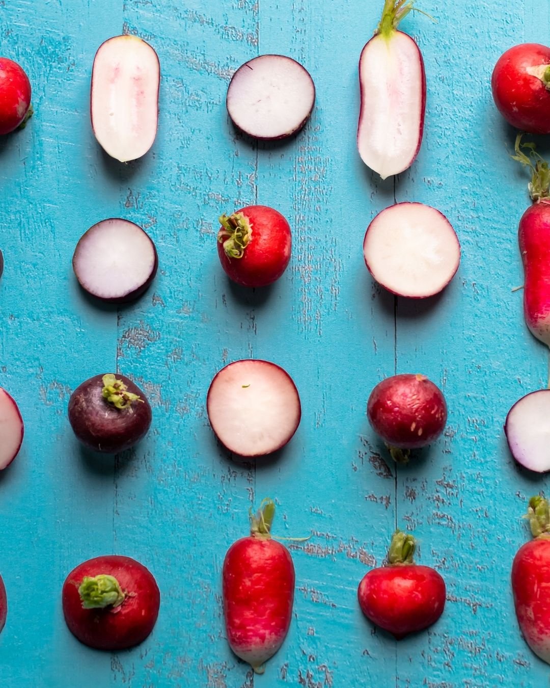 Radishes halved and whole, laid out in a grid on turquoise painted wood, shot overhead