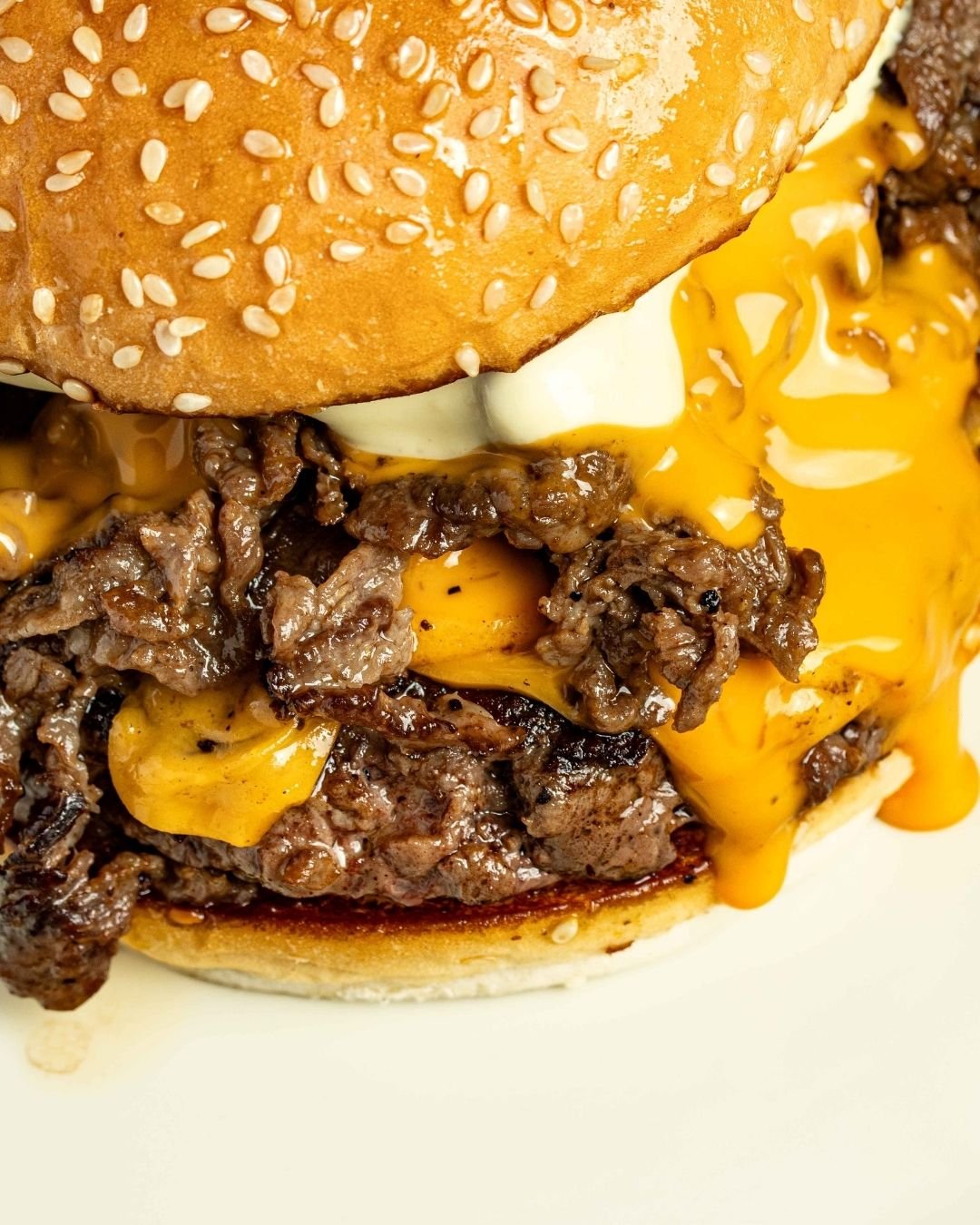 Close-up of a steak sandwich on a sesame bun, melted cheese running down the side
