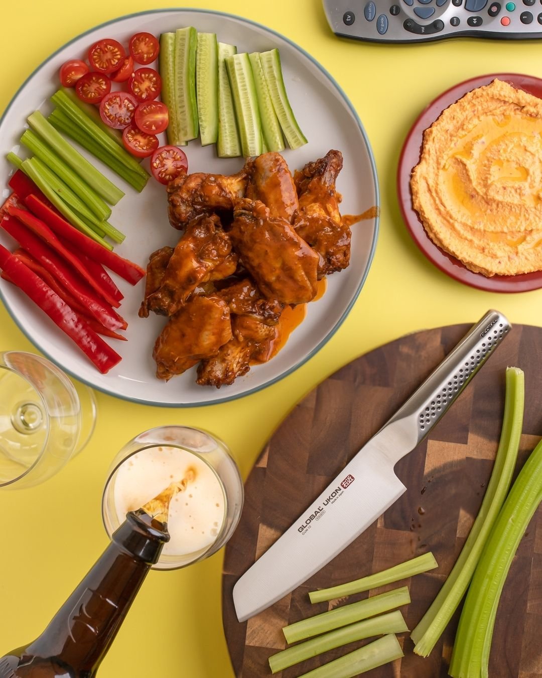 Overhead of buffalo wings with celery, cucumber and hummus, beer being poured, Global Ukon knife