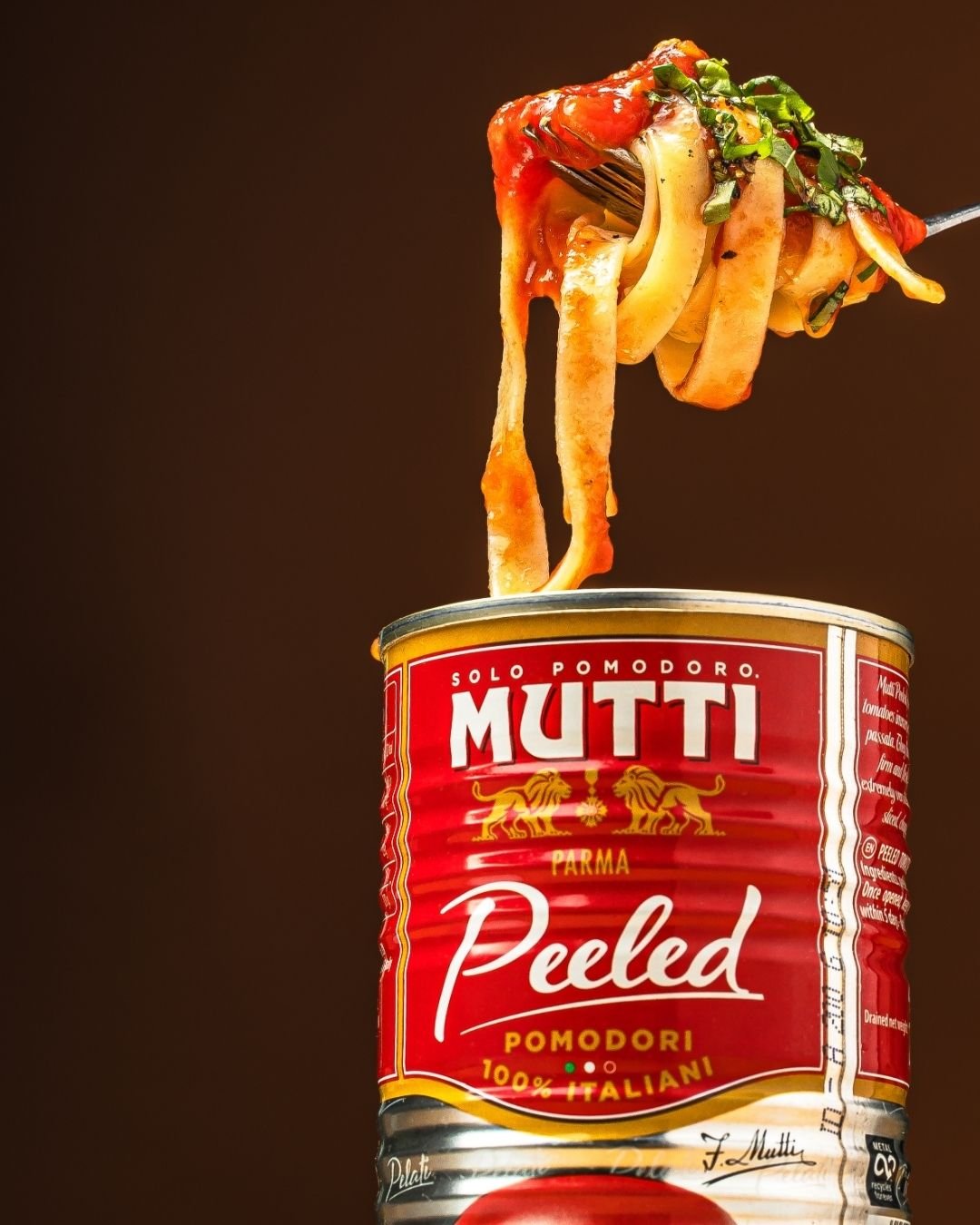Forkful of tagliatelle in tomato sauce lifted above an open tin of peeled tomatoes