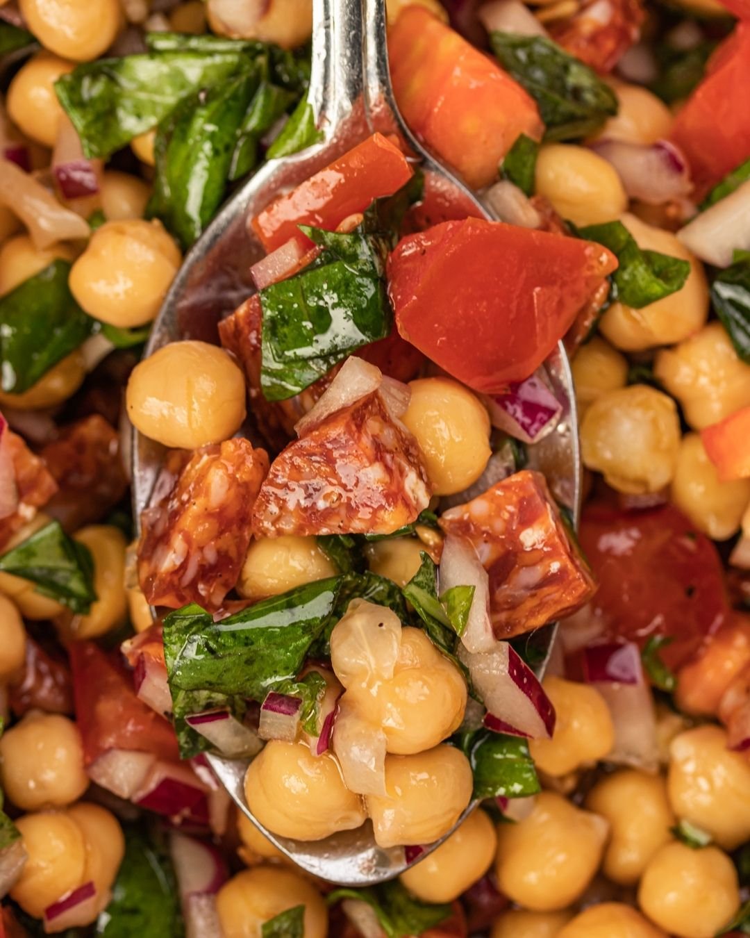 Close-up of chickpea salad with chorizo and tomato, lifted on a spoon