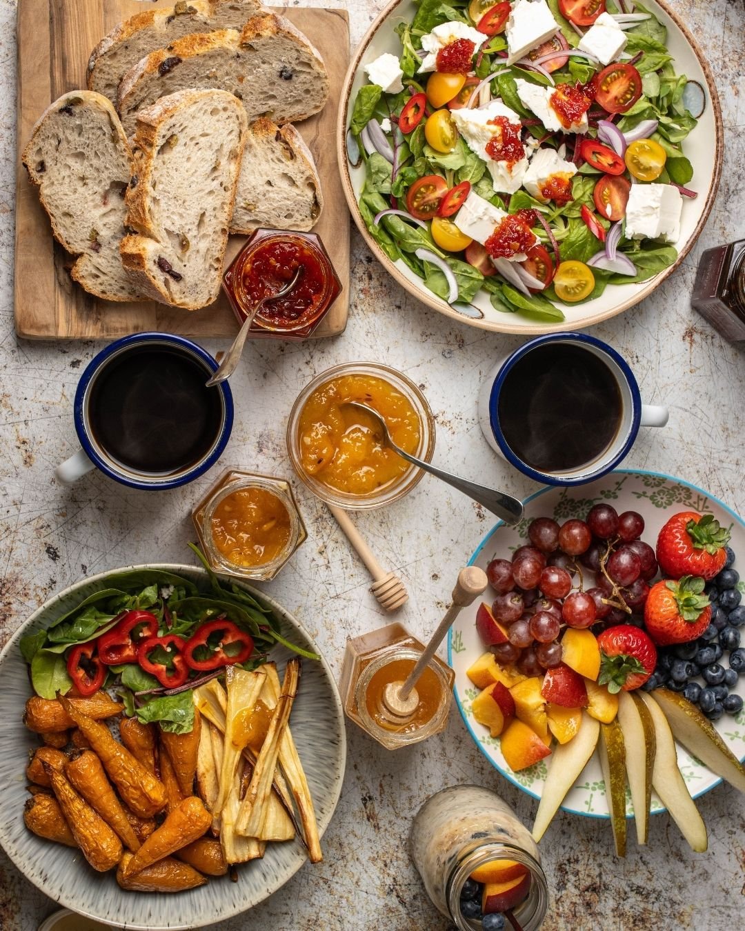 Overhead brunch spread with sourdough, salad, roast carrots and parsnips, fruit, jams and coffee