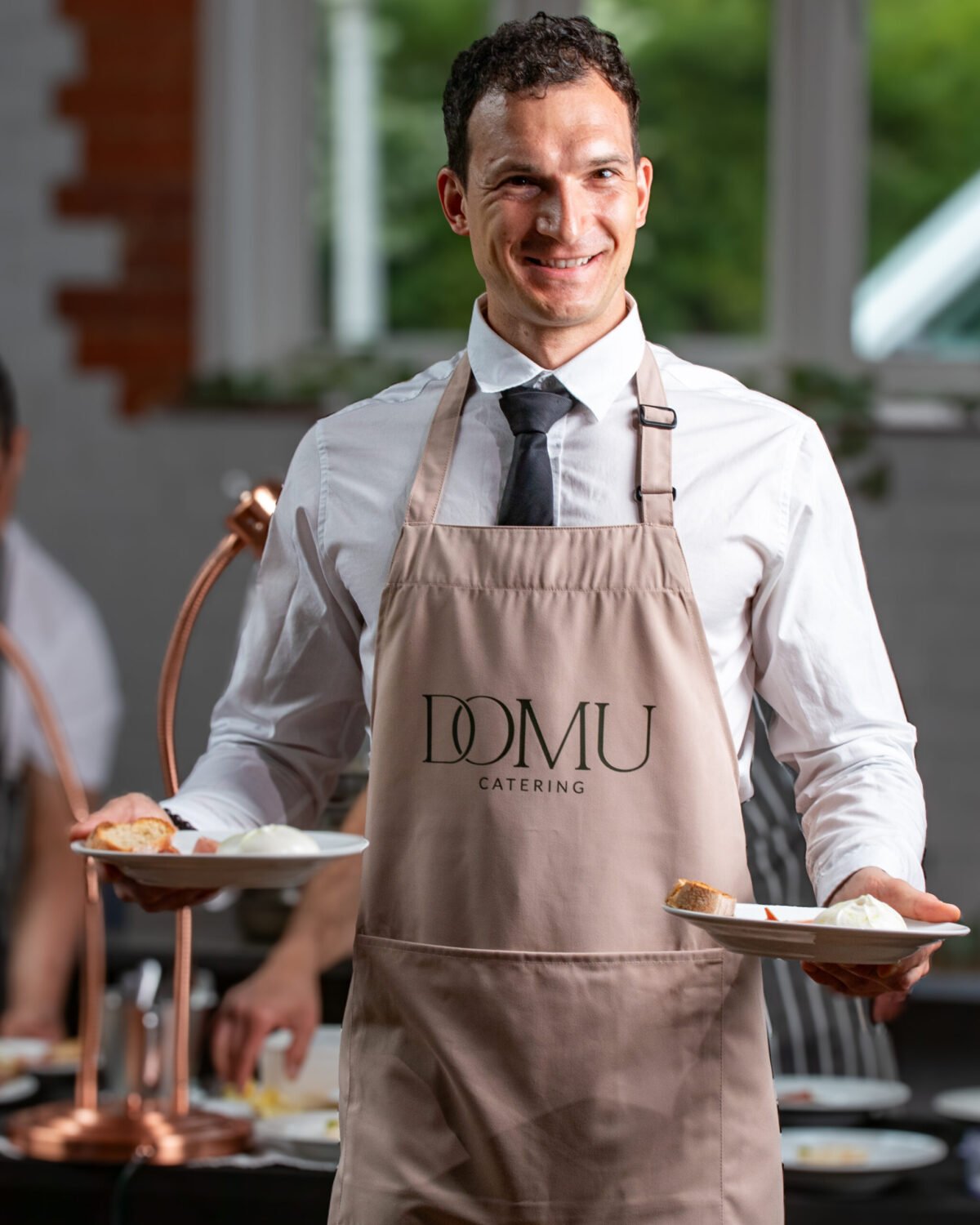 Waiter in a branded apron carrying two plated desserts through a service