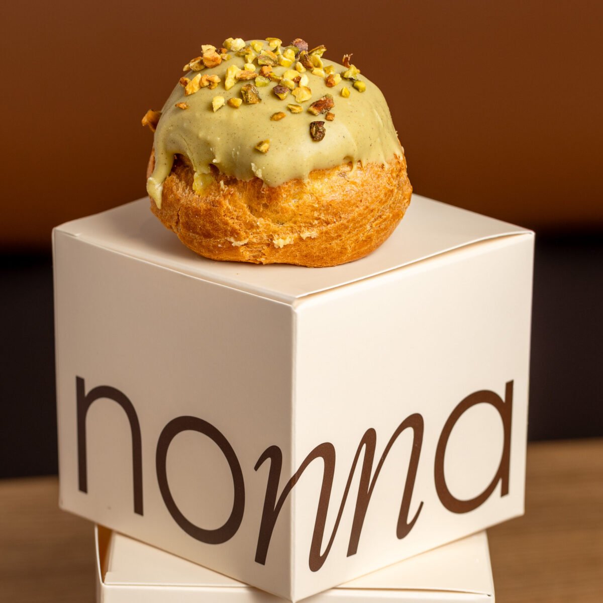 Pistachio choux bun on a bakery box, warm light against a dark brown background