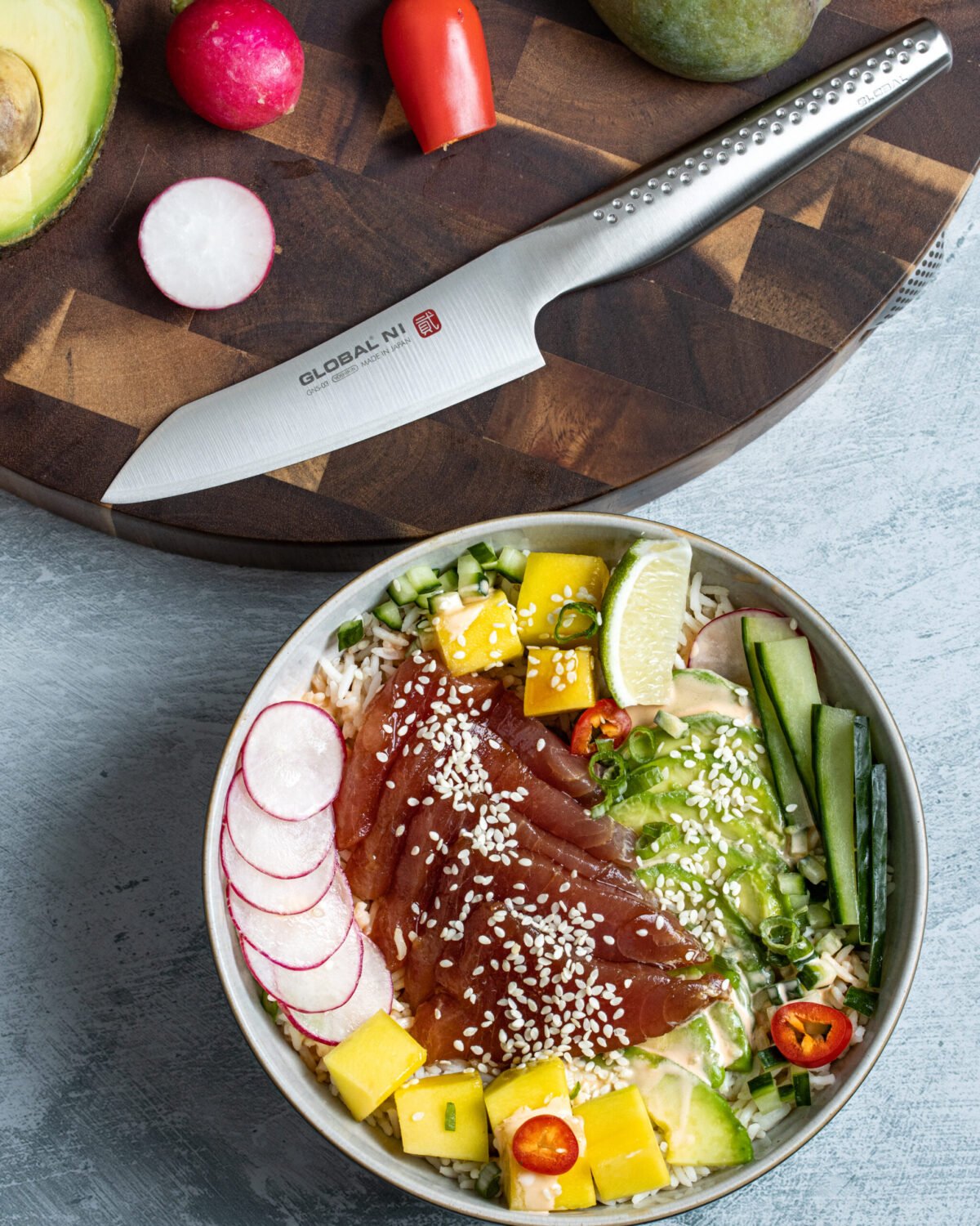 Poke bowl of cured tuna, mango, cucumber and radish with a Global NI knife on the board