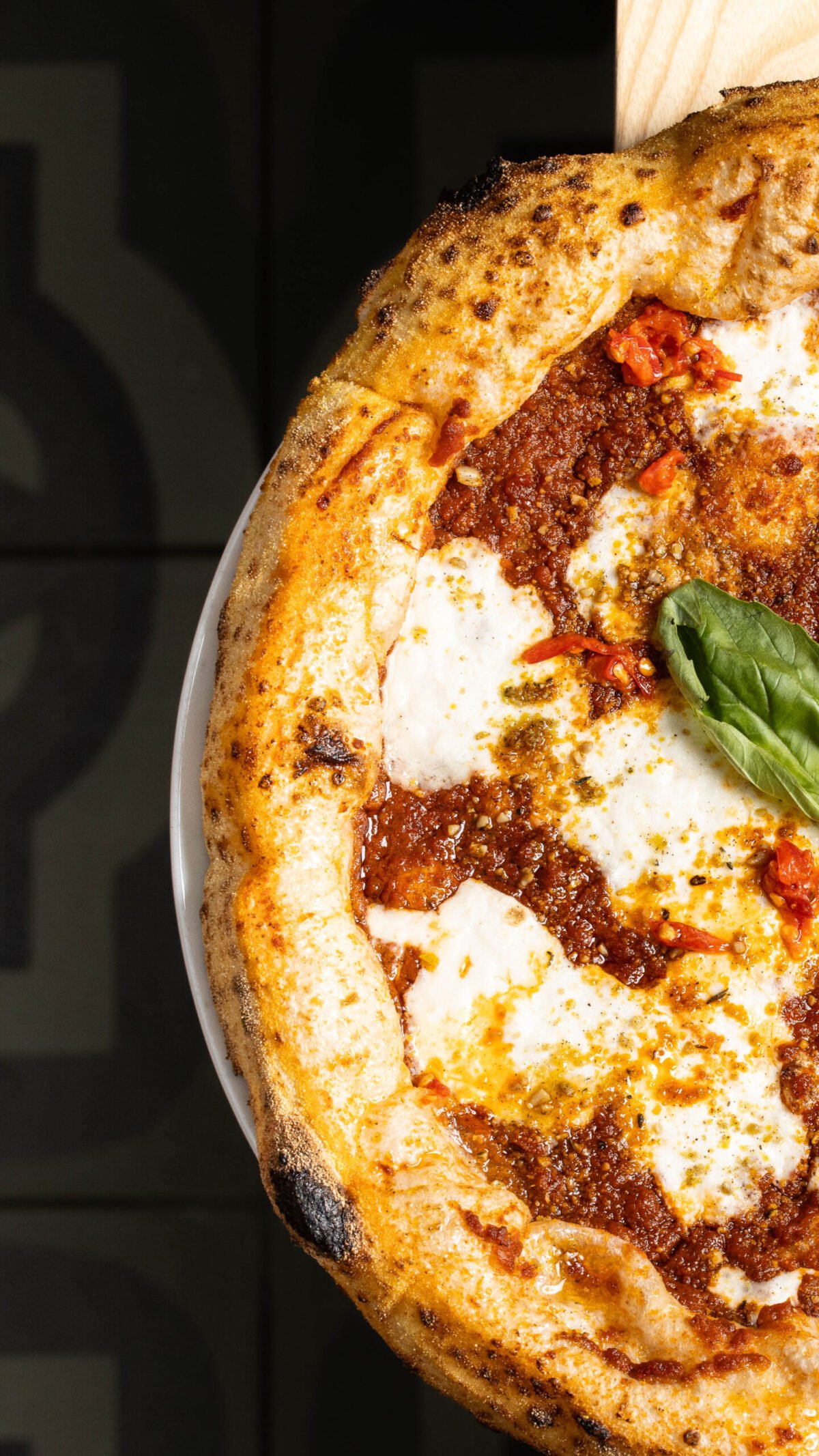Close-up of a wood fired Purezza pizza with ragu, mozzarella and basil lifted on a peel
