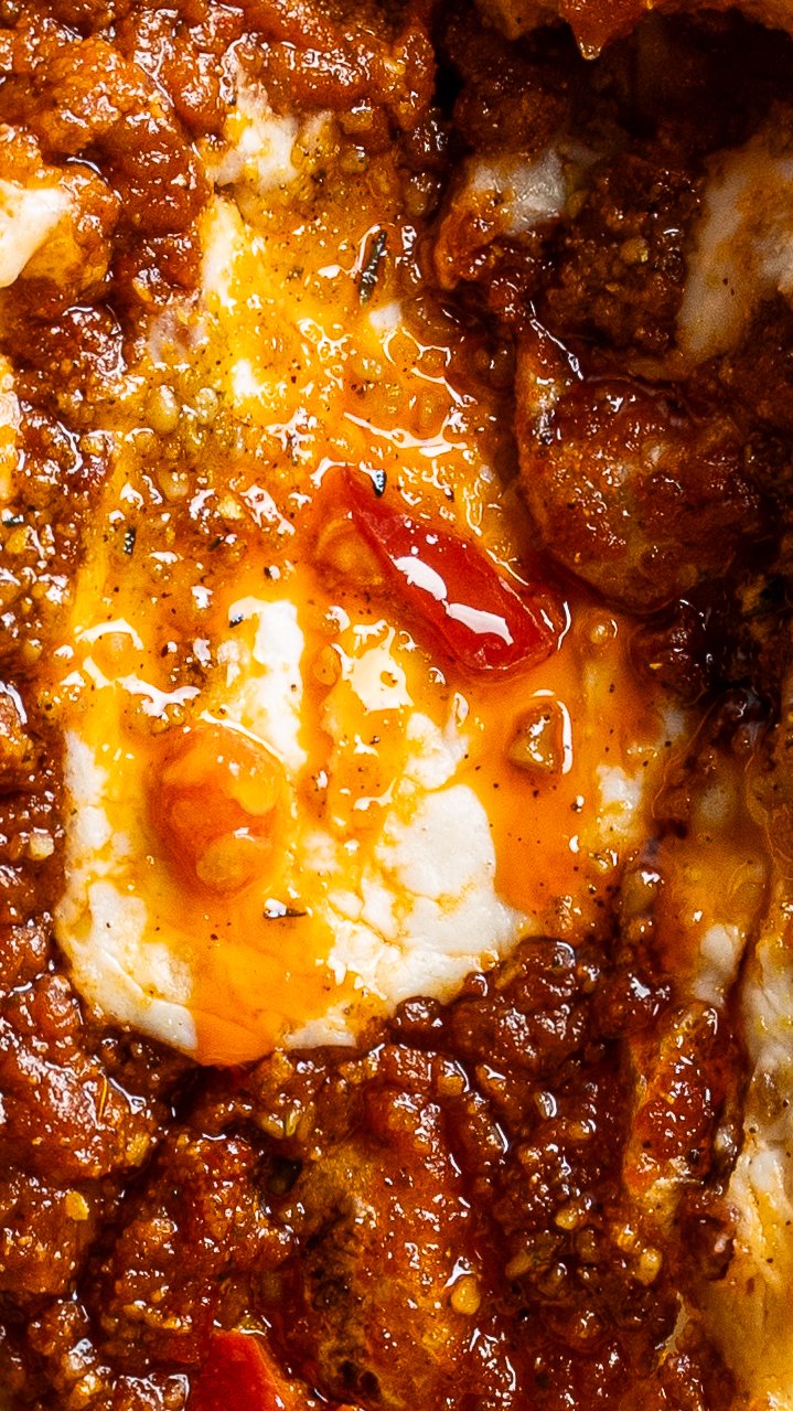 Extreme close-up of baked ragu and melted mozzarella, oil pooling on the surface