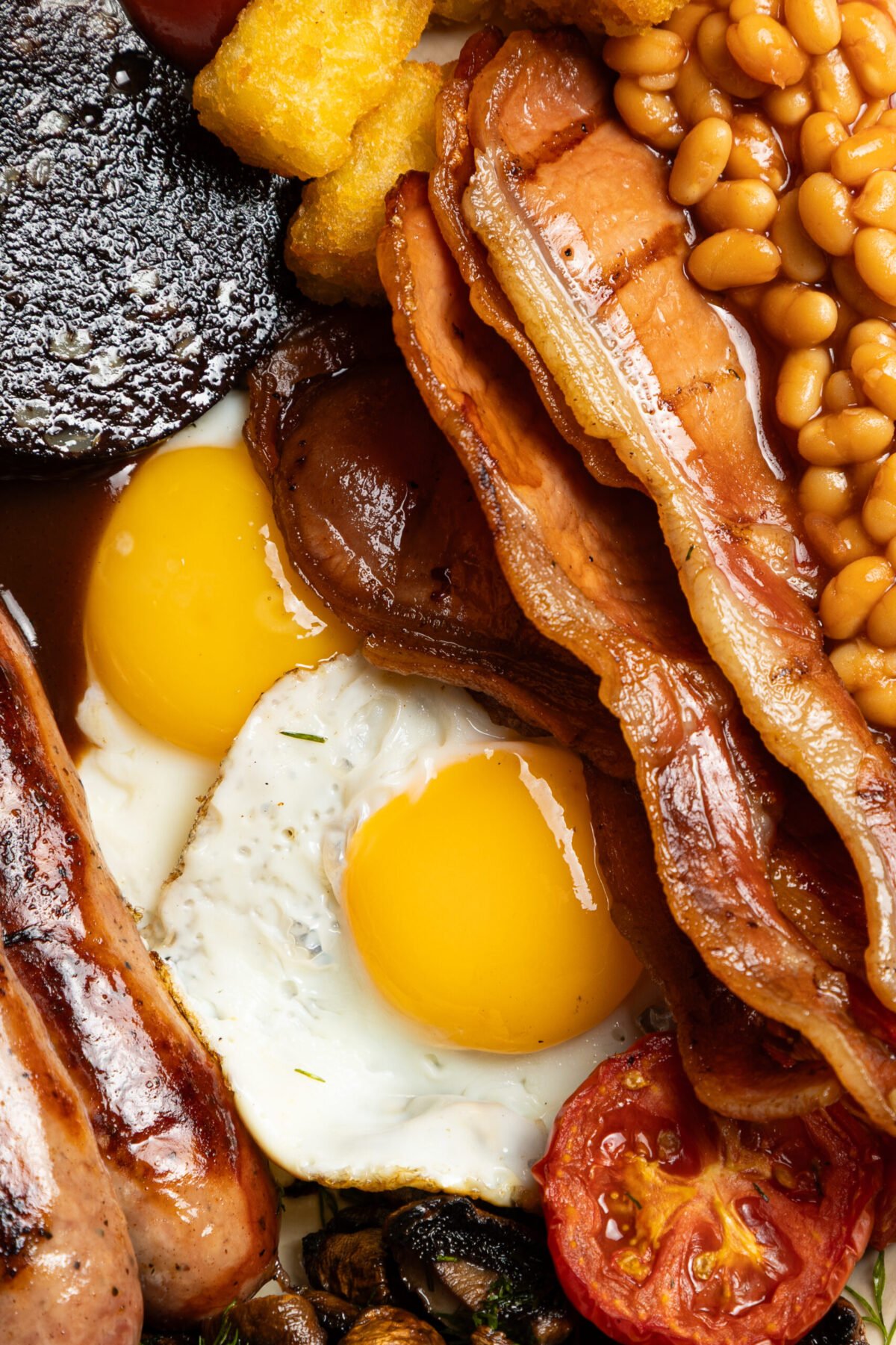 Close-up full English breakfast with bacon, fried eggs, beans, sausage and black pudding