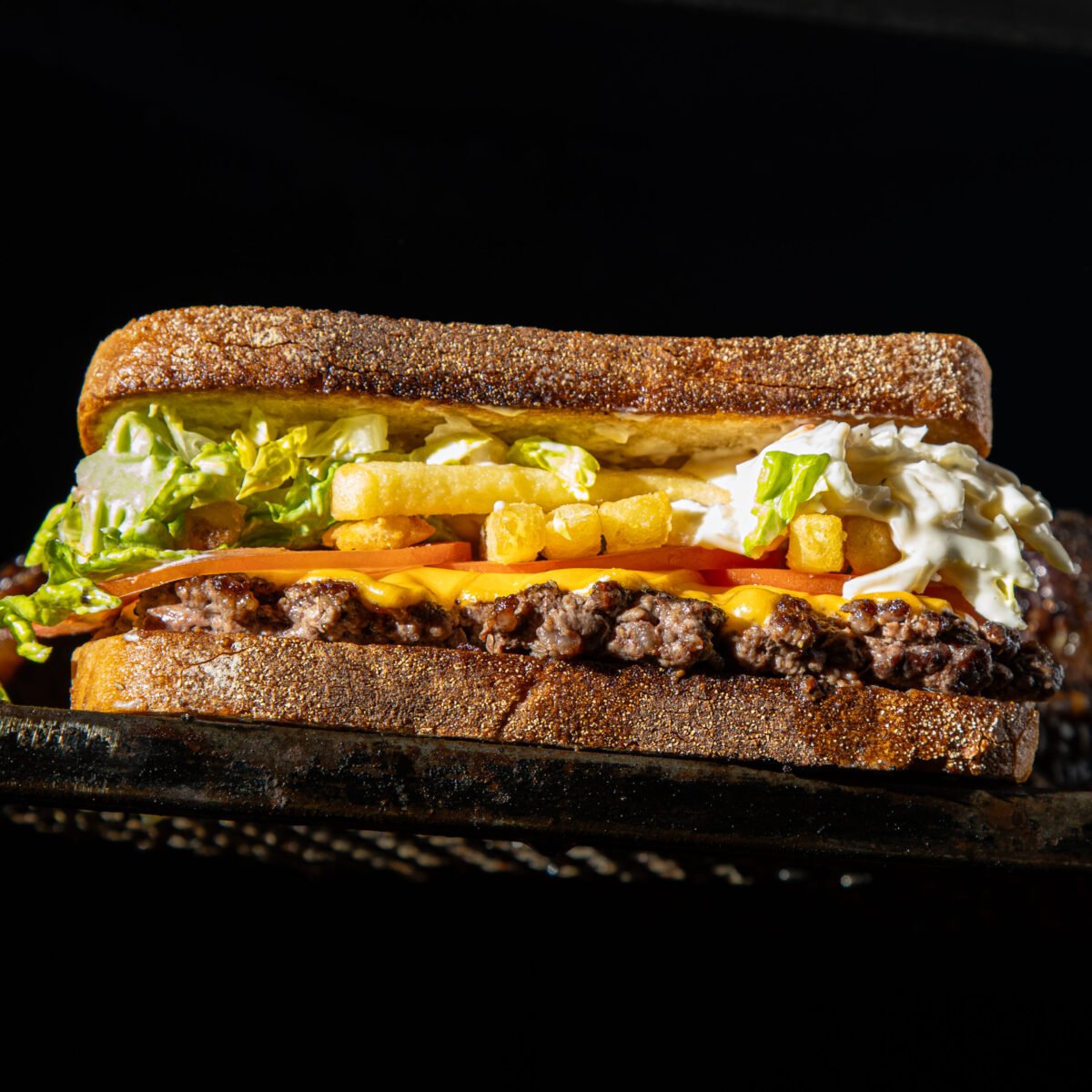 Red Dog Saloon burger in toasted bread with fries, lettuce, tomato and slaw, lit against black