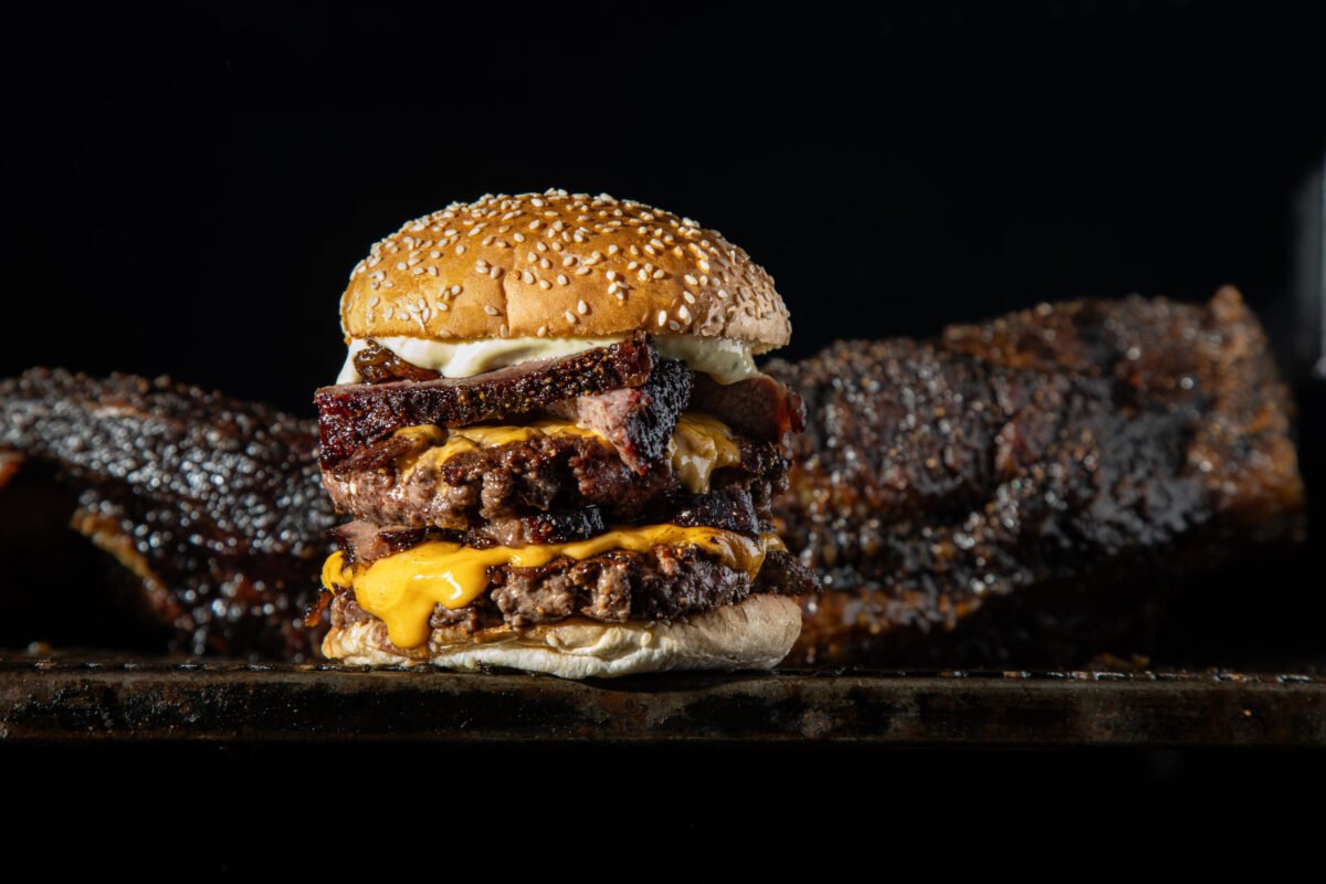 Red Dog Saloon double cheeseburger with racks of smoked ribs behind it, low key lighting