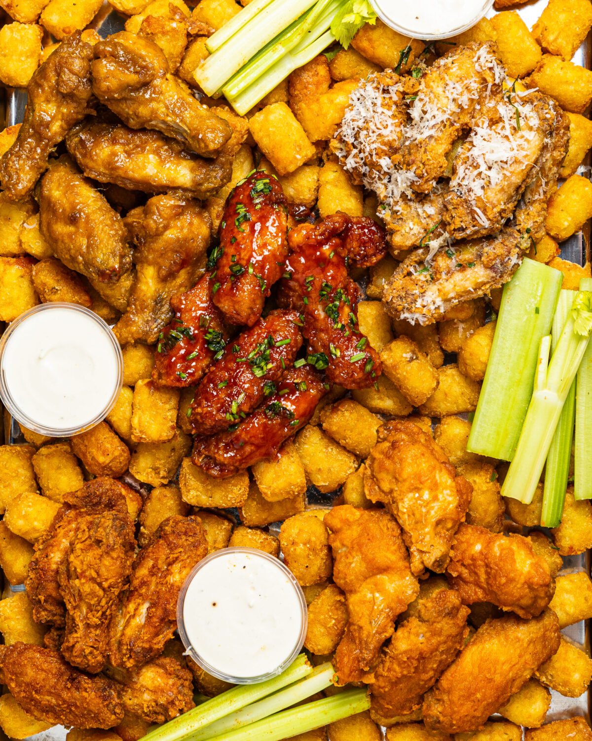 Overhead sharing tray of chicken wings in four coatings with tater tots, celery and dips