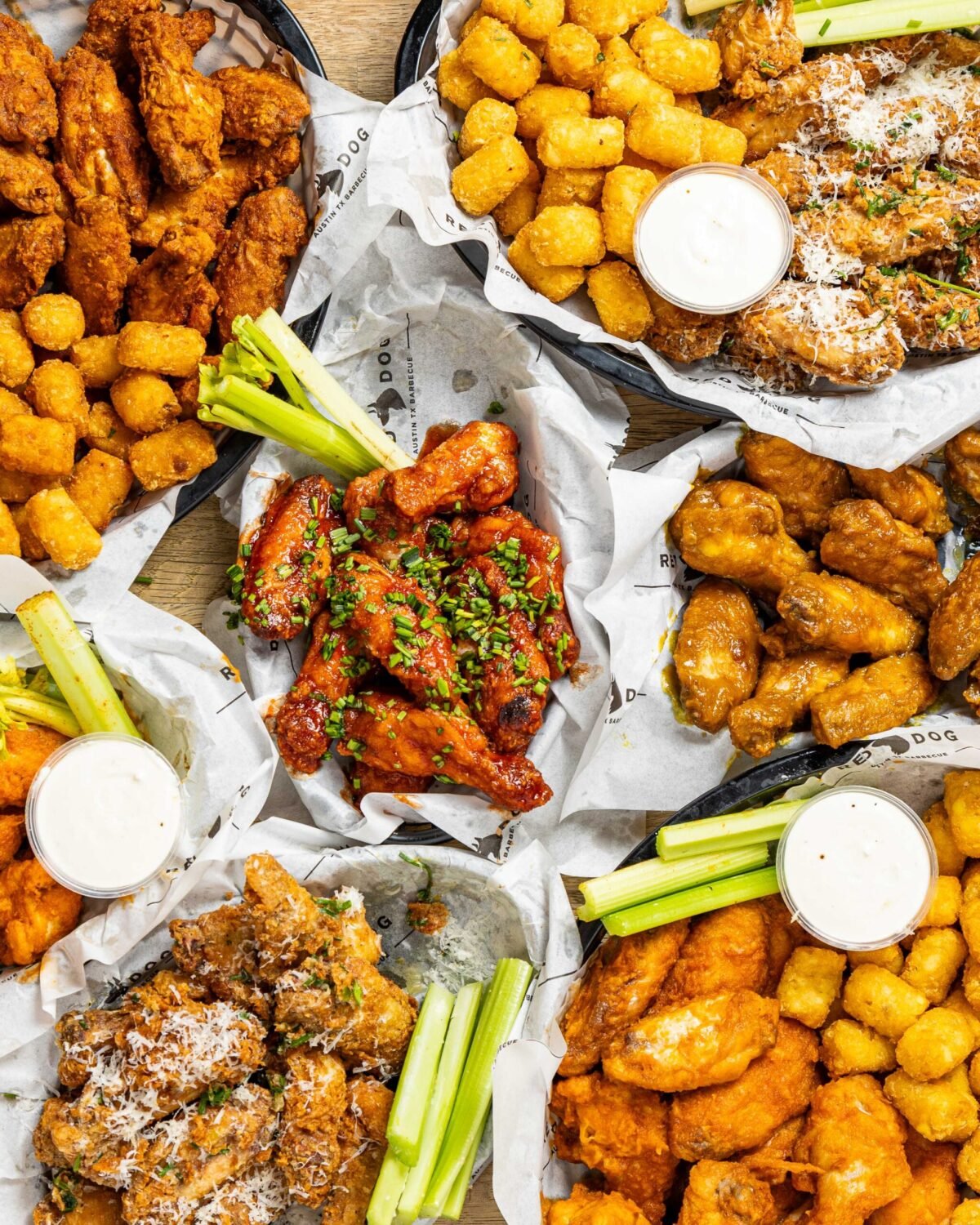 Overhead of five baskets of chicken wings in different coatings with tater tots and dips
