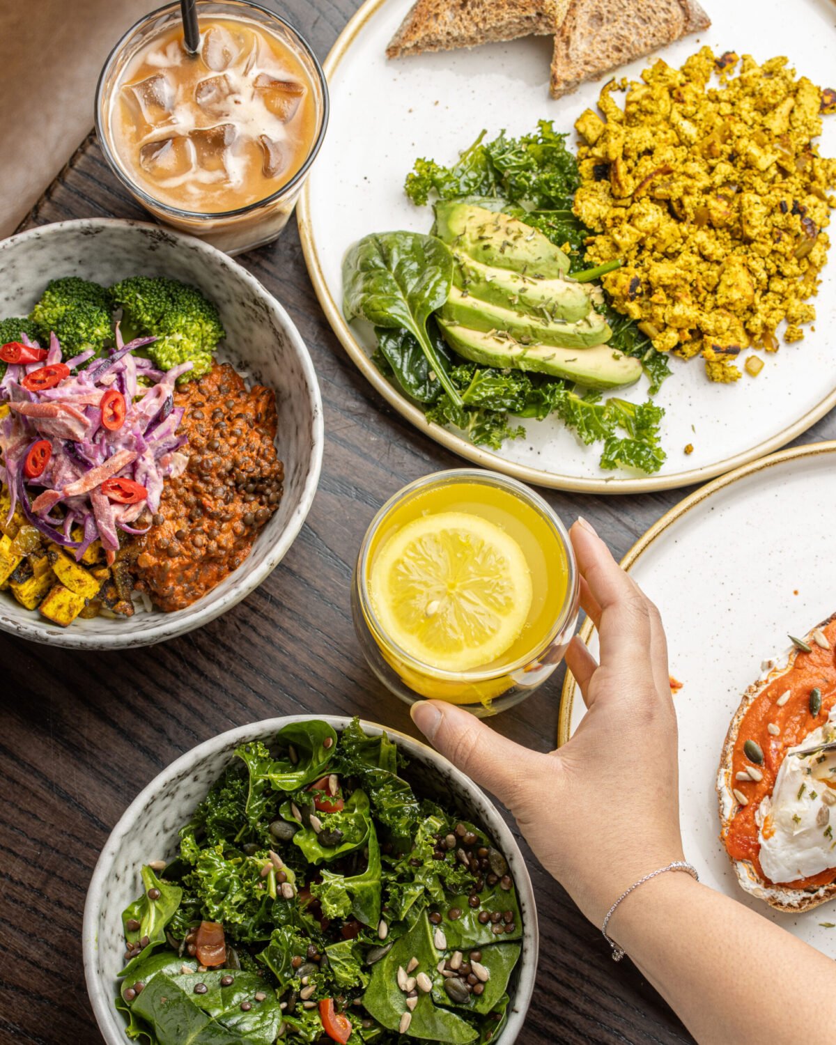 Overhead vegan brunch spread with tofu scramble, kale salad, iced coffee and hot lemon