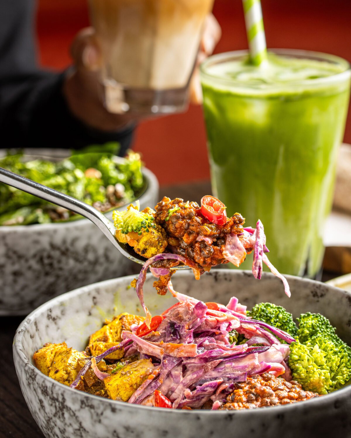Forkful of lentil ragu and red cabbage slaw lifted from a bowl, green smoothie behind