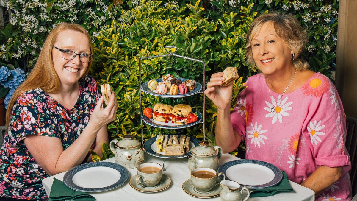 Two guests raising sandwiches at an outdoor afternoon tea table