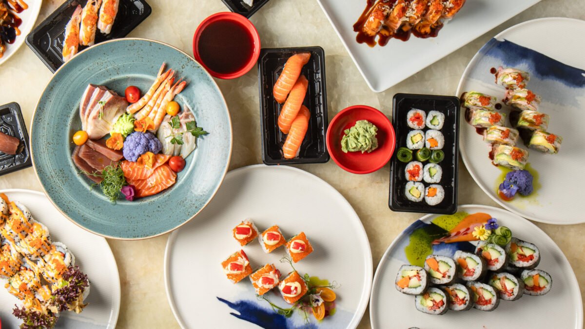 Overhead spread of sashimi, nigiri and maki rolls across several plates with soy and wasabi