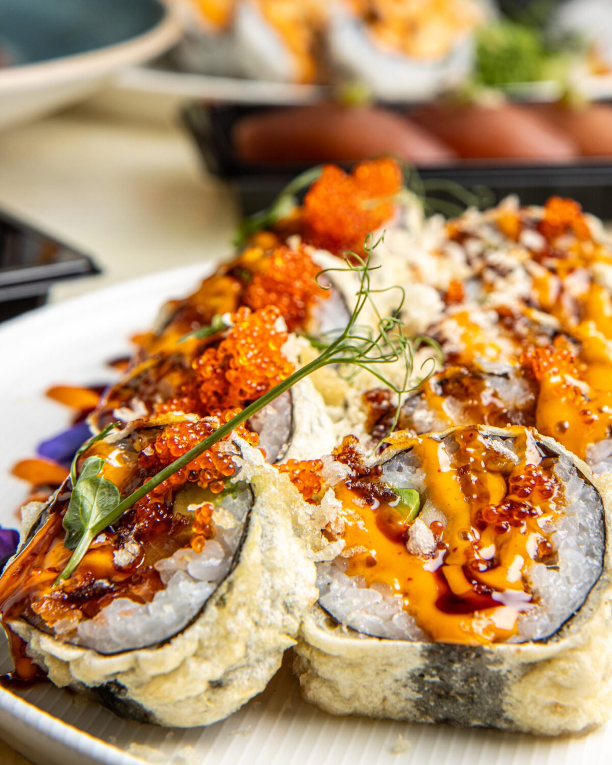Close-up of tempura maki topped with roe, sriracha mayo and micro herbs