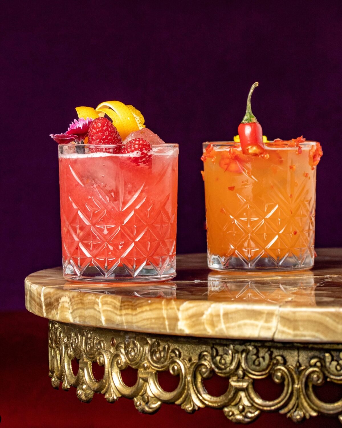Two cut crystal cocktails on an onyx stand, one raspberry and one chilli rimmed