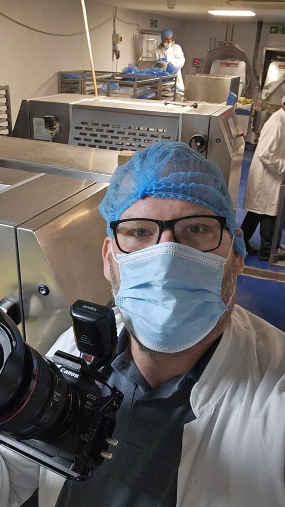 Photographing on the Port Royal factory floor in hairnet, mask and coat, production line behind