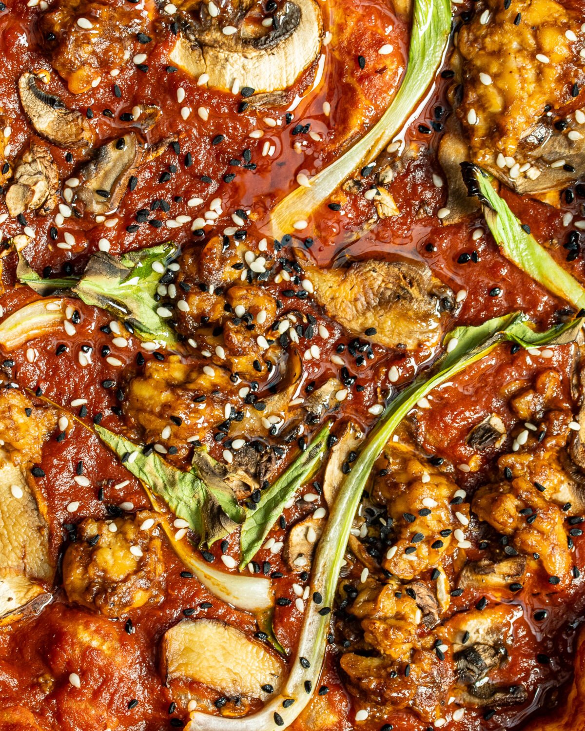 Macro of a pizza surface with sauce, mushroom, spring onion, sesame and nigella seeds