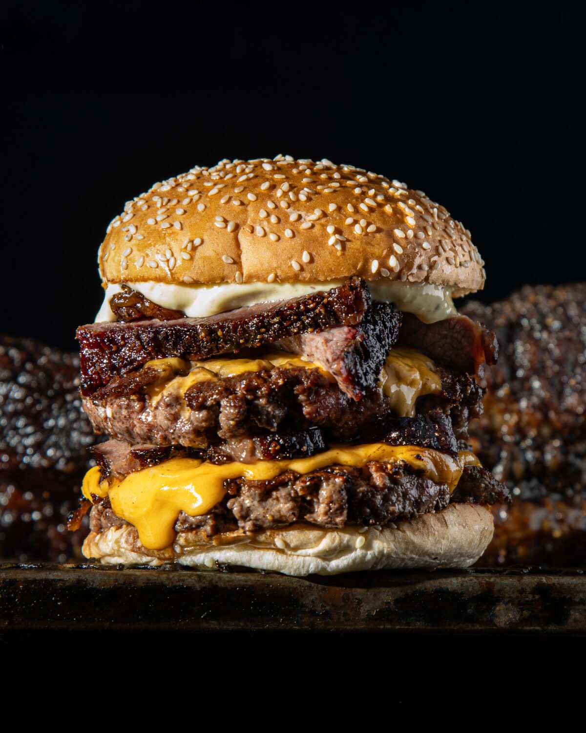 Brisket and double patty burger with melted cheese on black, ribs out of focus behind