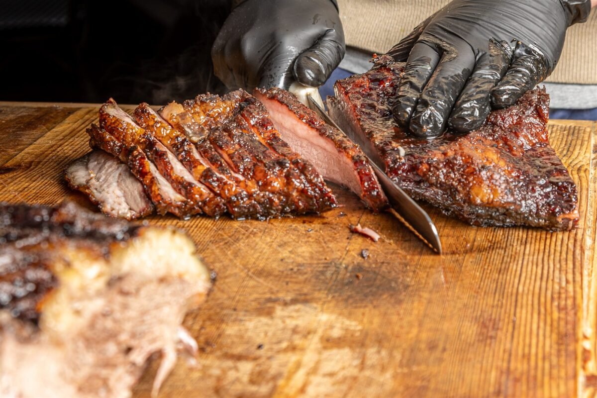 Gloved hands slicing a smoked brisket on a wooden board