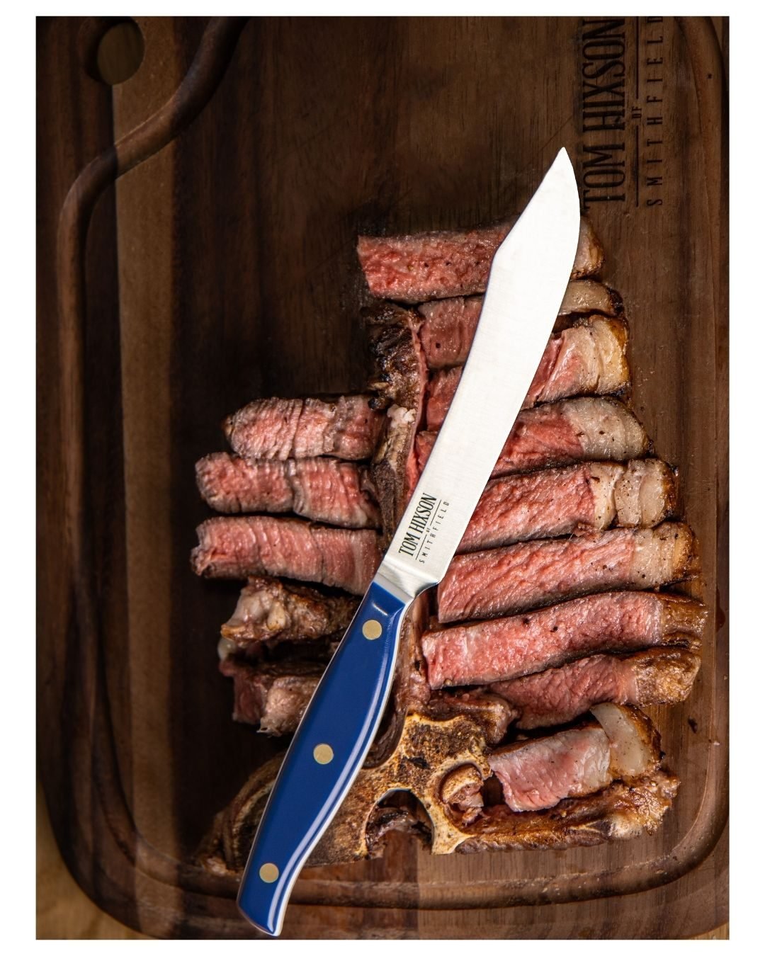 Sliced rare steak fanned across a wooden board with a blue-handled steak knife laid over it