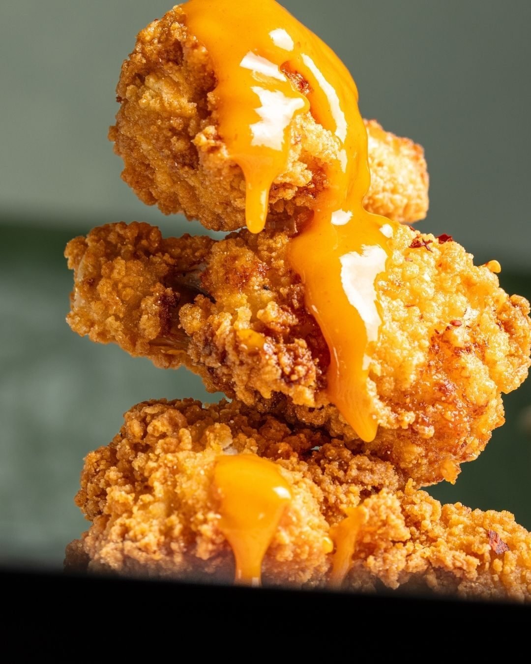 Stack of fried chicken strips with cheese sauce dripping down the side