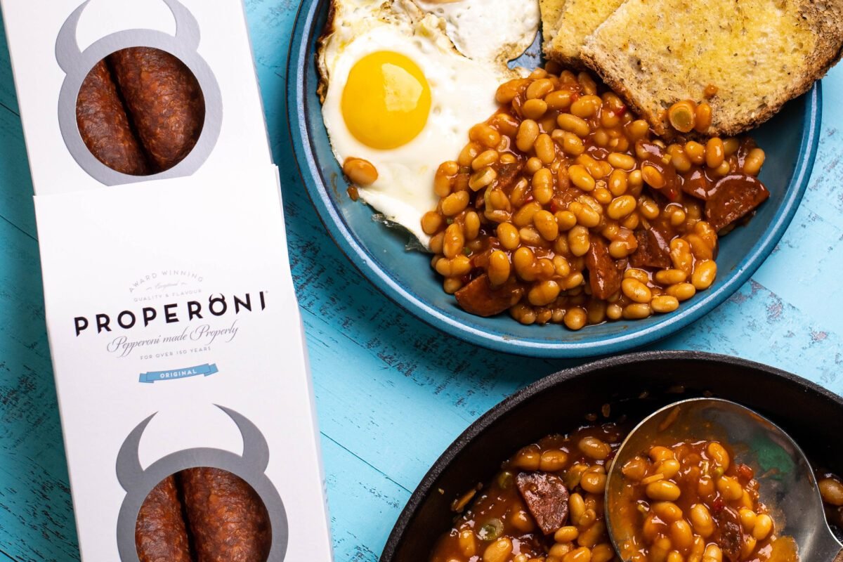 Properoni pack beside a plate of baked beans, fried egg and toast on a blue painted surface