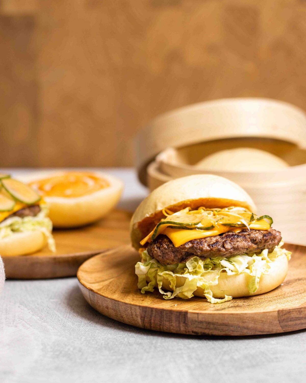 Bao burger with pickles and shredded lettuce on a wooden plate, bamboo steamer behind