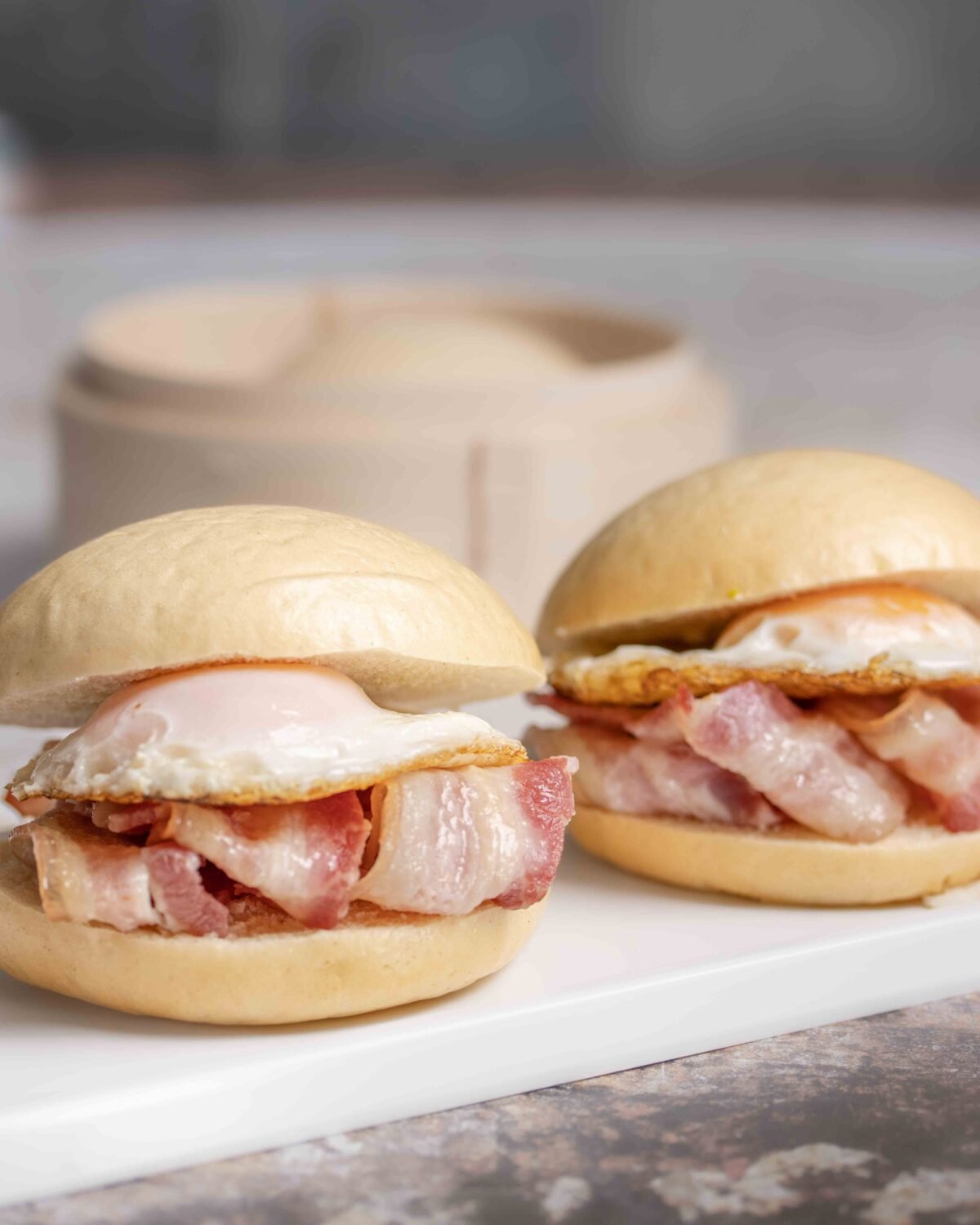 Two bacon and fried egg bao buns served on a white ceramic plate