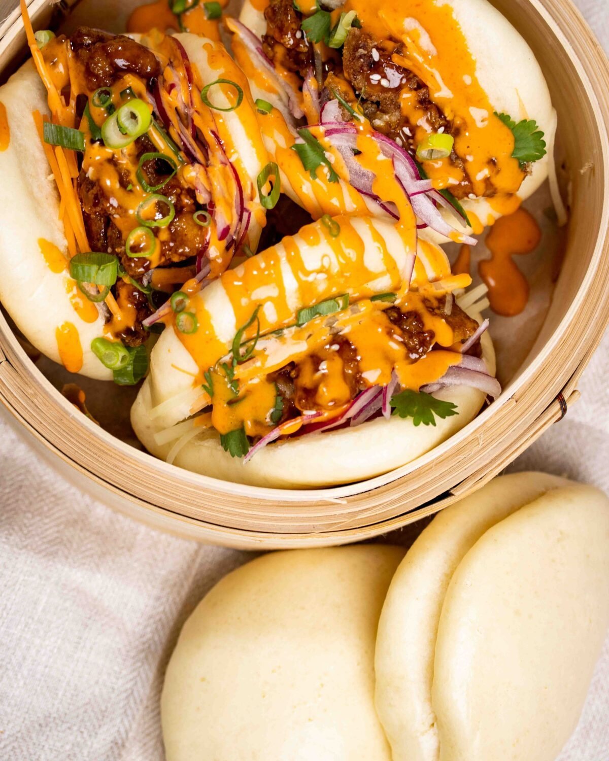 Bao buns filled with pulled meat, sriracha and pickled red onion in a bamboo steamer basket