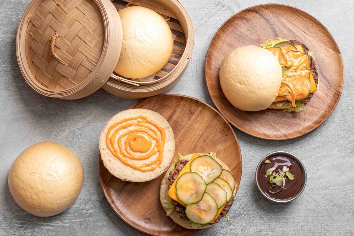 Overhead bao burgers and plain steamed buns arranged on round wooden plates