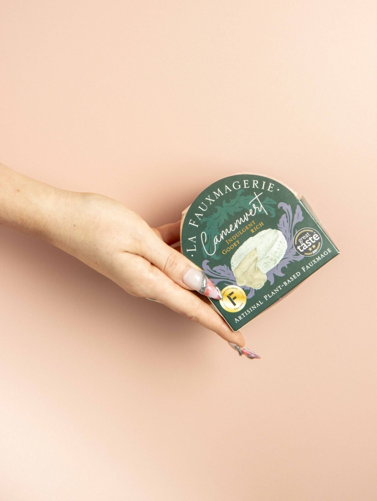 Hand holding a boxed camembert against a soft pink background