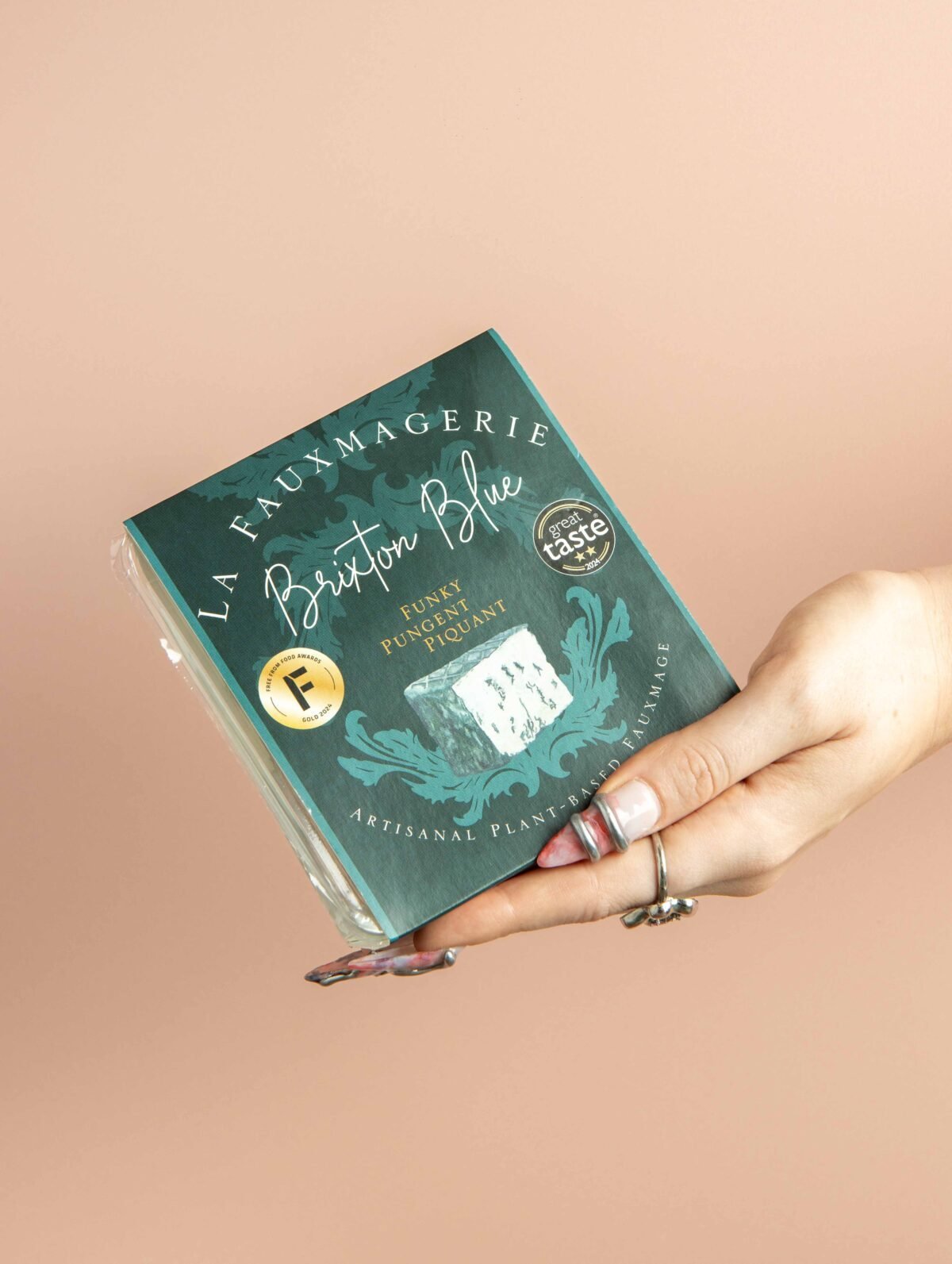Hand holding a boxed artisan blue cheese against a soft pink background