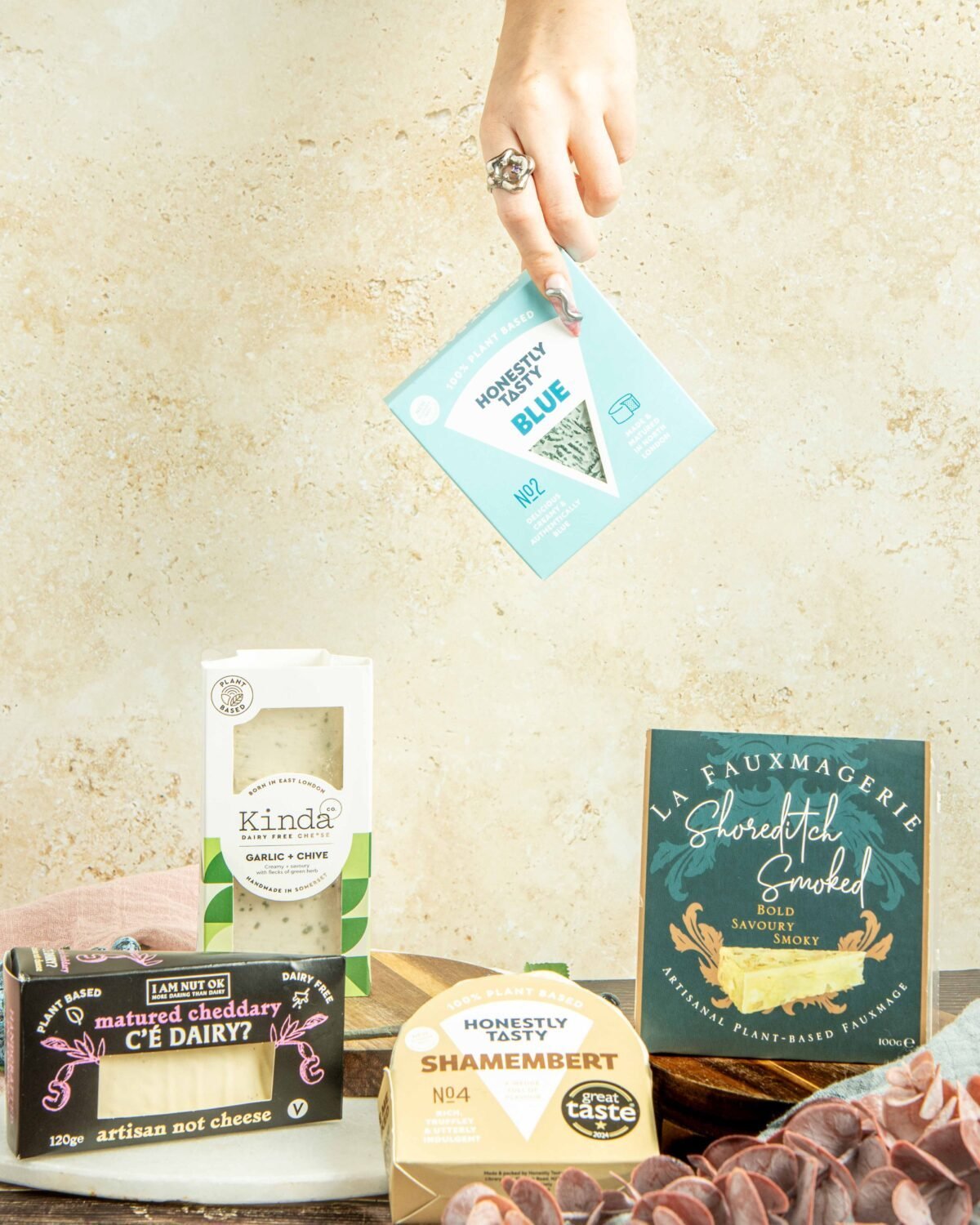 Hand placing a cheese pack above an arrangement of artisan cheese packaging on stone