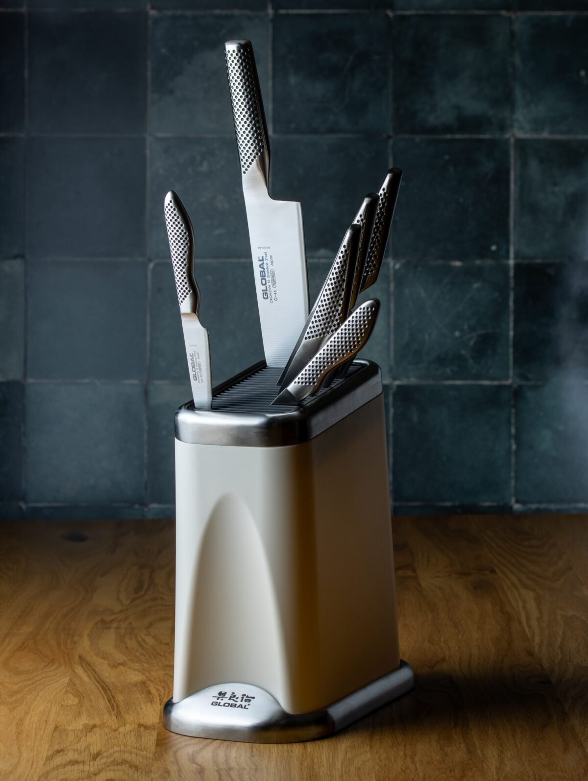 Global knife block holding a full set of knives against dark green kitchen tiles
