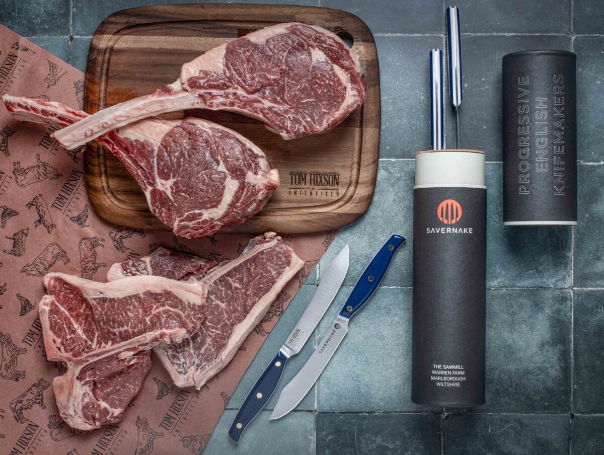 Overhead rib steaks on a Tom Hixson board with steak knives and English charcuterie tubes on slate