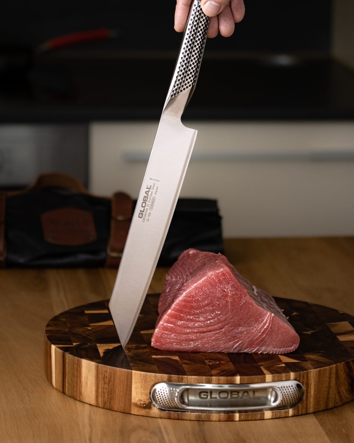 Hand lowering a Global knife towards a tuna loin on a round end-grain chopping block