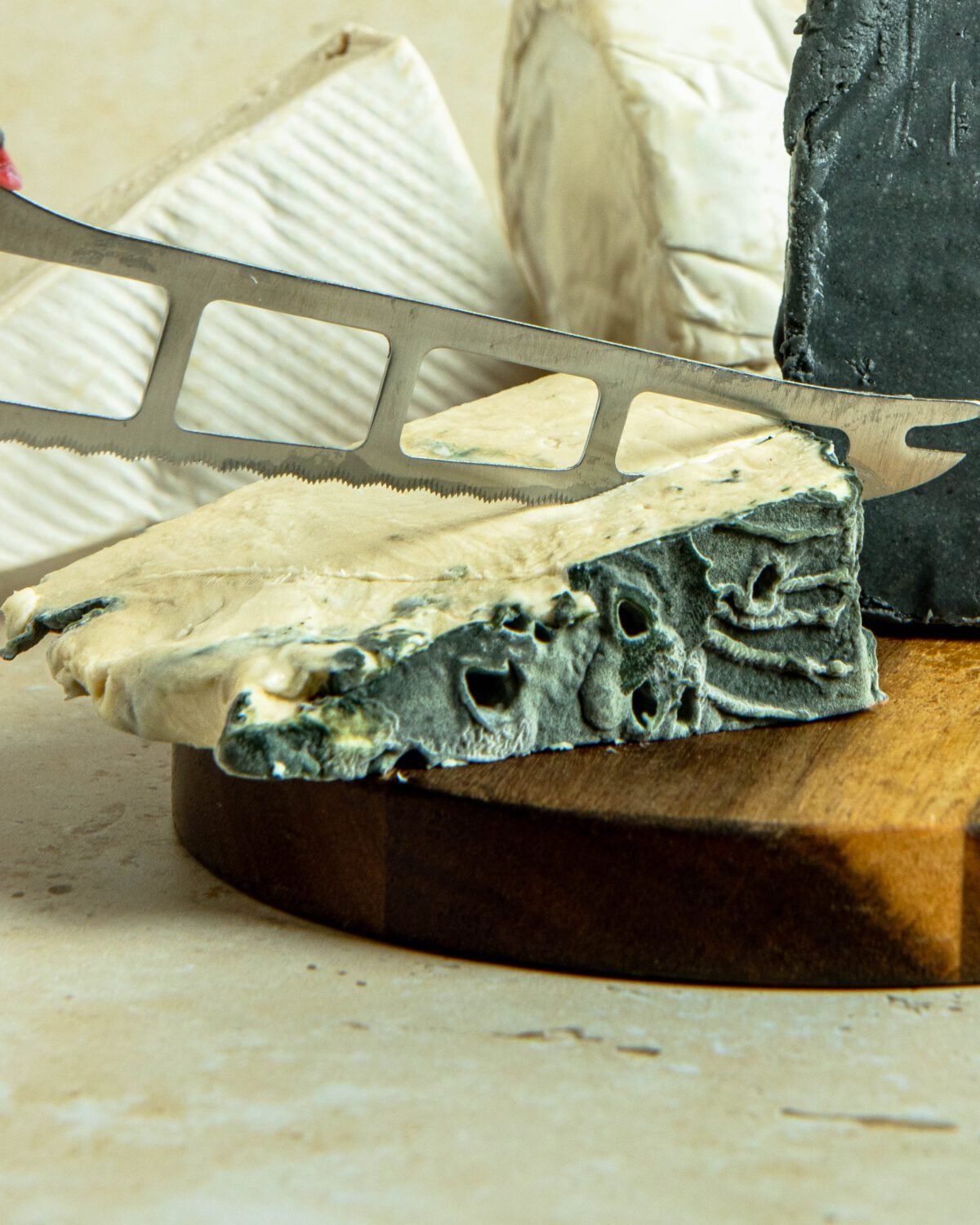 Cheese knife cutting through a wedge of ash-rinded soft cheese on a board