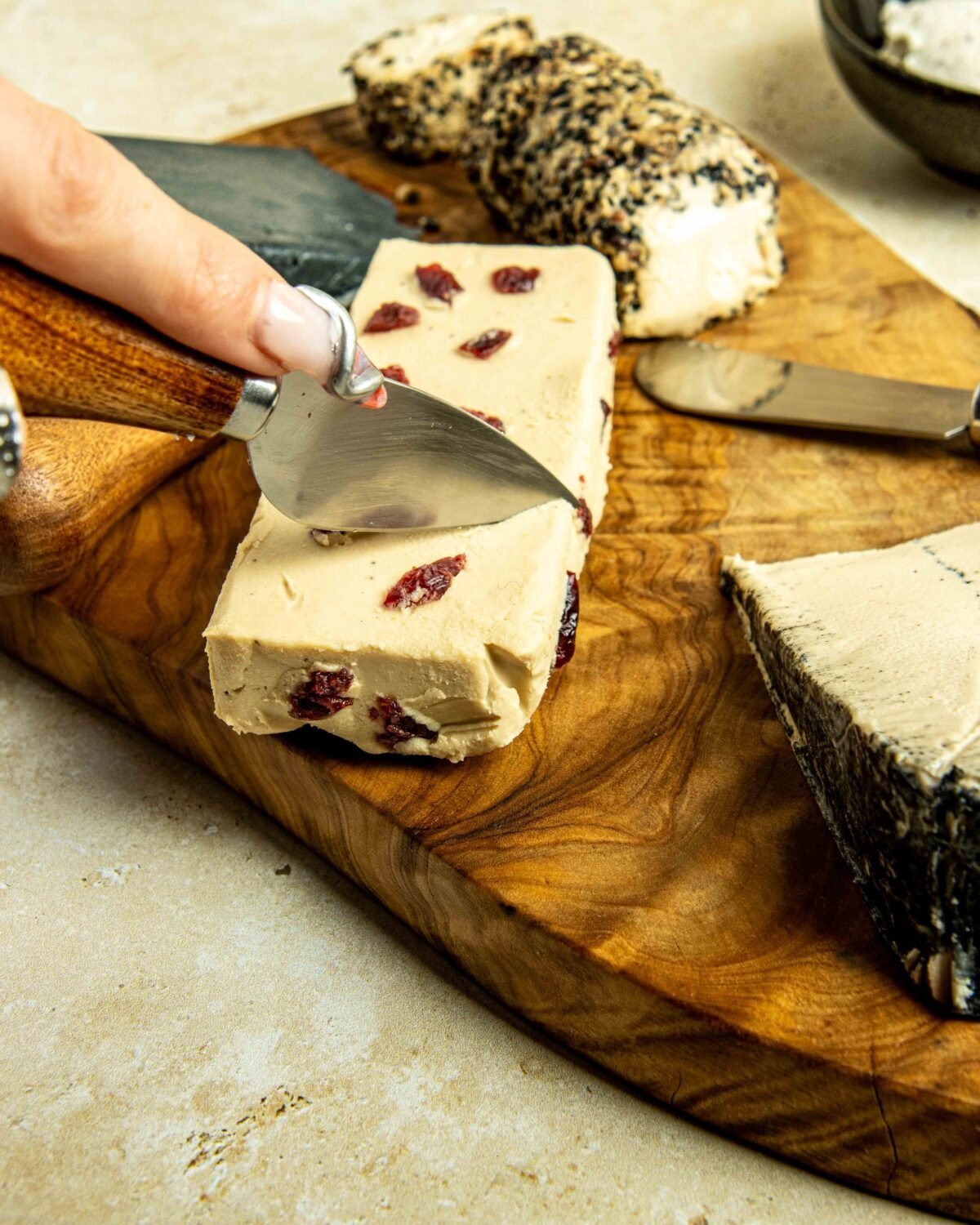 Hand cutting a slice of cranberry-studded cheese on an olive wood board