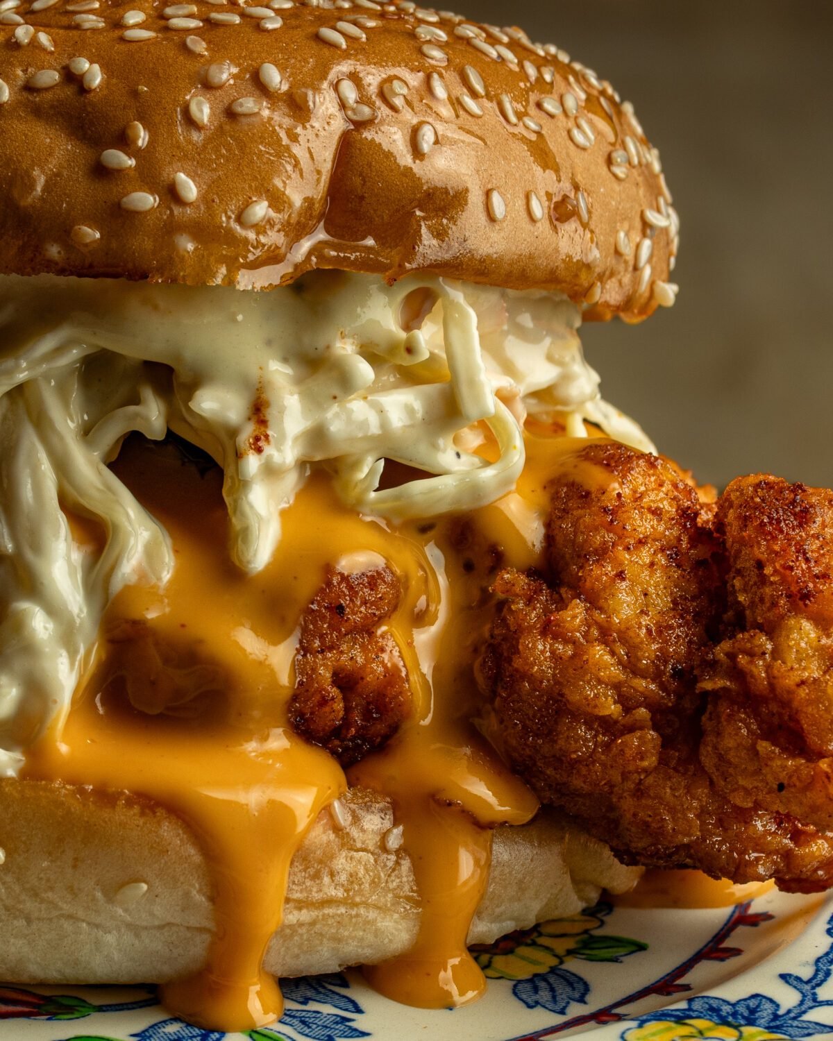 Fried chicken burger with slaw and cheese sauce spilling from a sesame seed bun