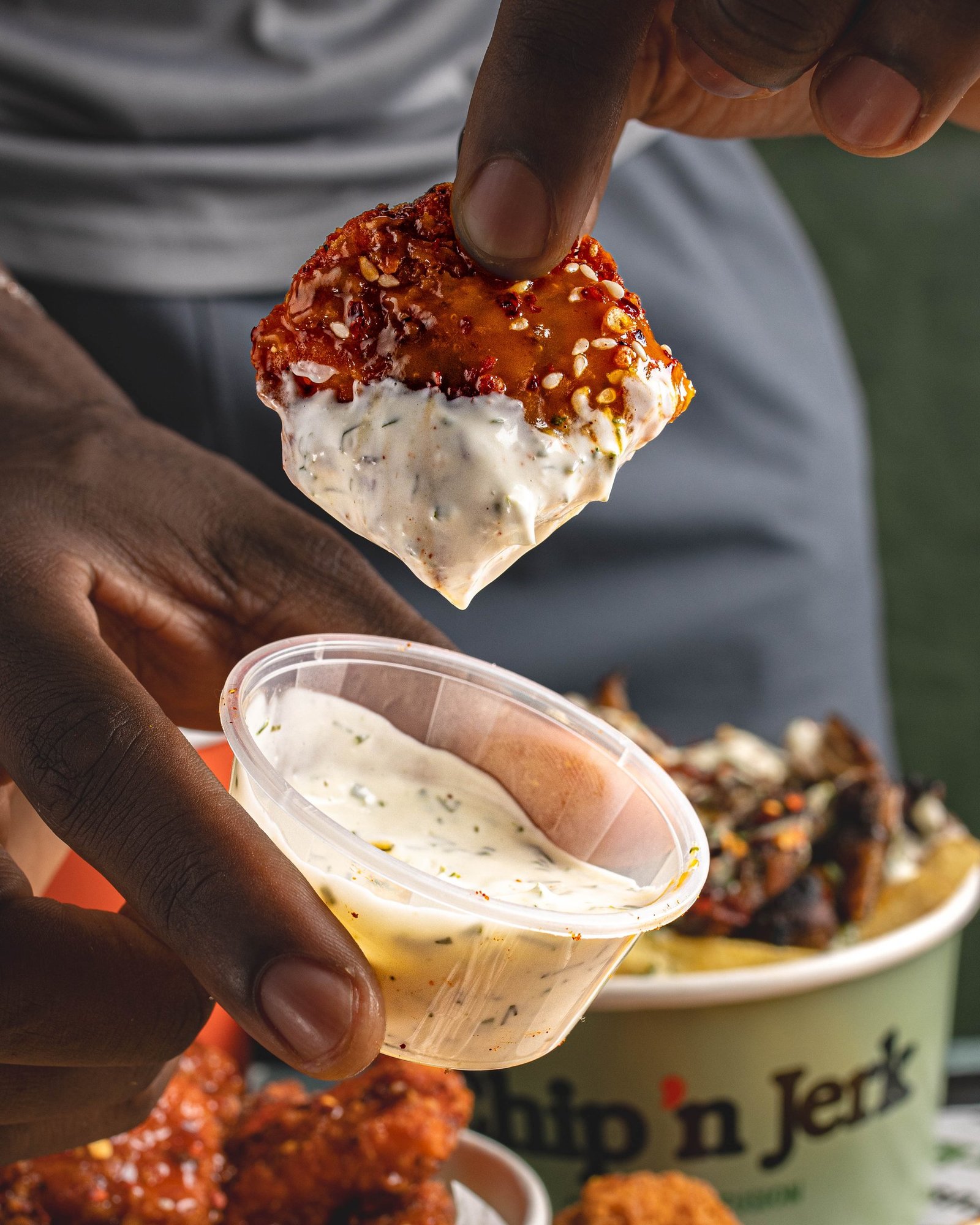 A piece of sauced Caribbean chicken lifted out of a pot of herb dip and held to camera, lifestyle food photography for a QSR in Holloway, North London.