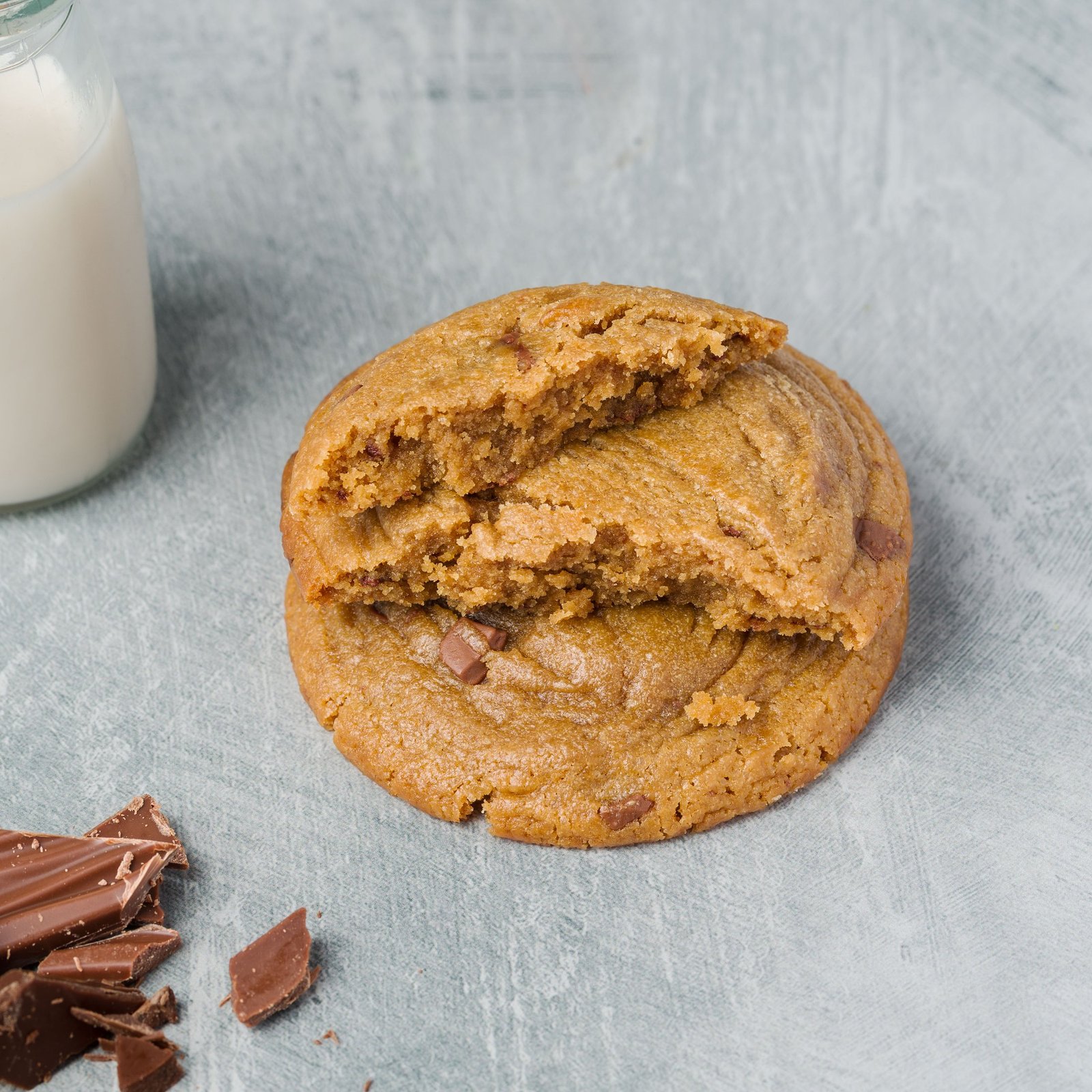 Chocolate chunk cookie broken open and stacked to show the crumb, with a bottle of milk and chocolate shards, from a food photography shoot for an artisan cookie brand in Croydon.
