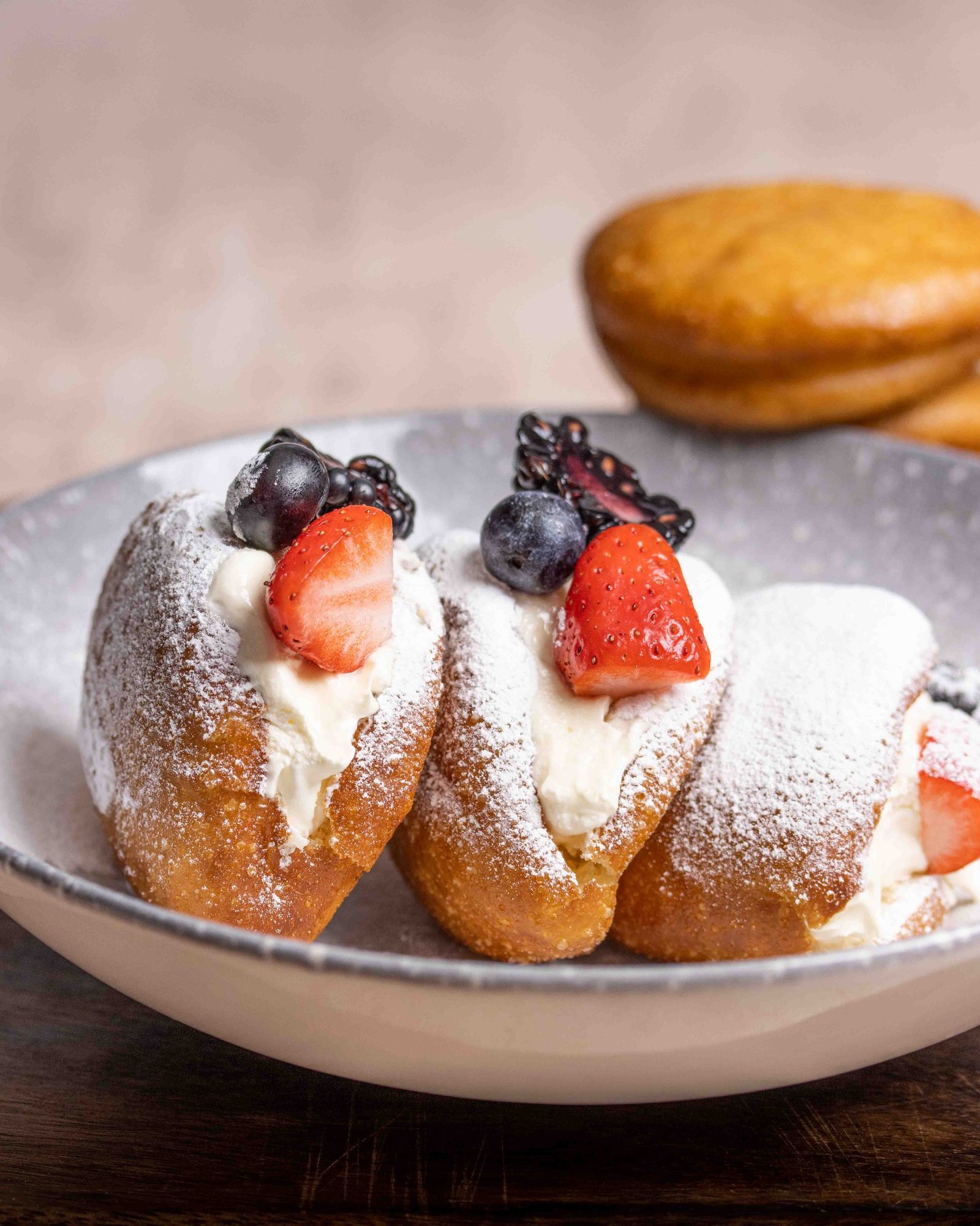 Two bao dusted with icing sugar and filled with whipped cream, topped with strawberry, blackberry and blueberry in a bowl, dessert food styling and photography for a bao manufacturer.