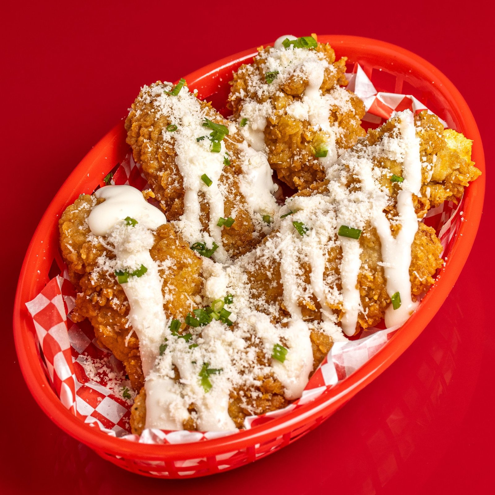 Fried chicken in a red basket on checked paper, finished with a white sauce drizzle, grated cheese and chives, delivery app photography for a chicken shop in Wood Green.